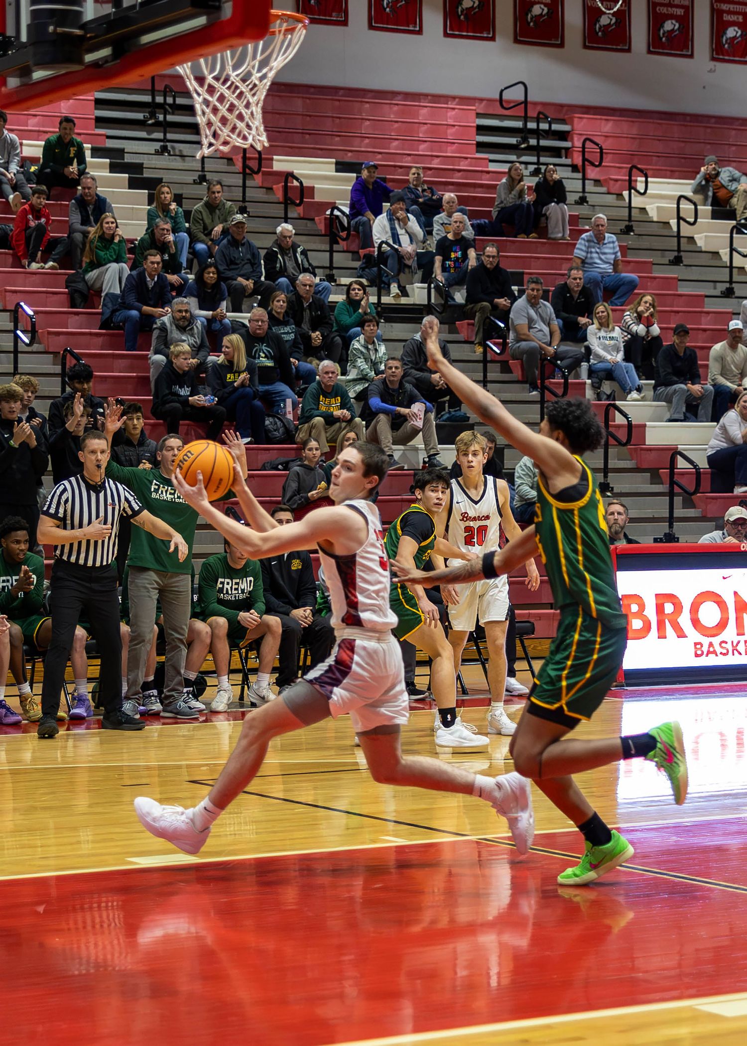 A high school basketball player drives to the hoop for a layup during a game in a packed gymnasium.