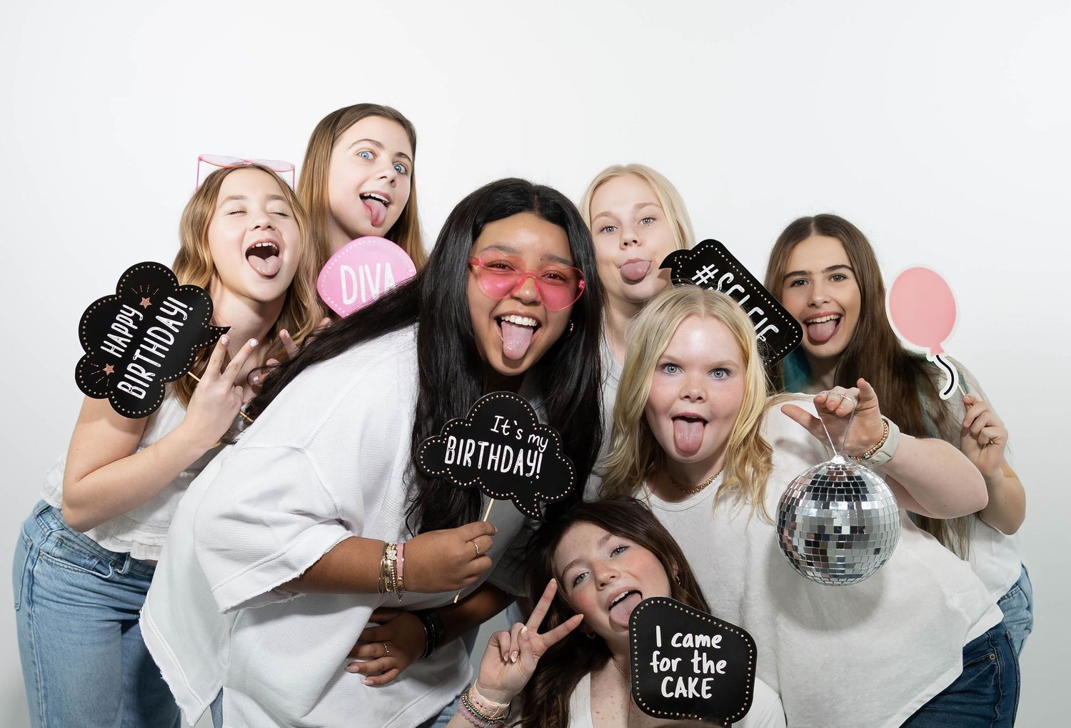 Group of teenage girls celebrating a birthday party with fun photo booth props and disco ball.