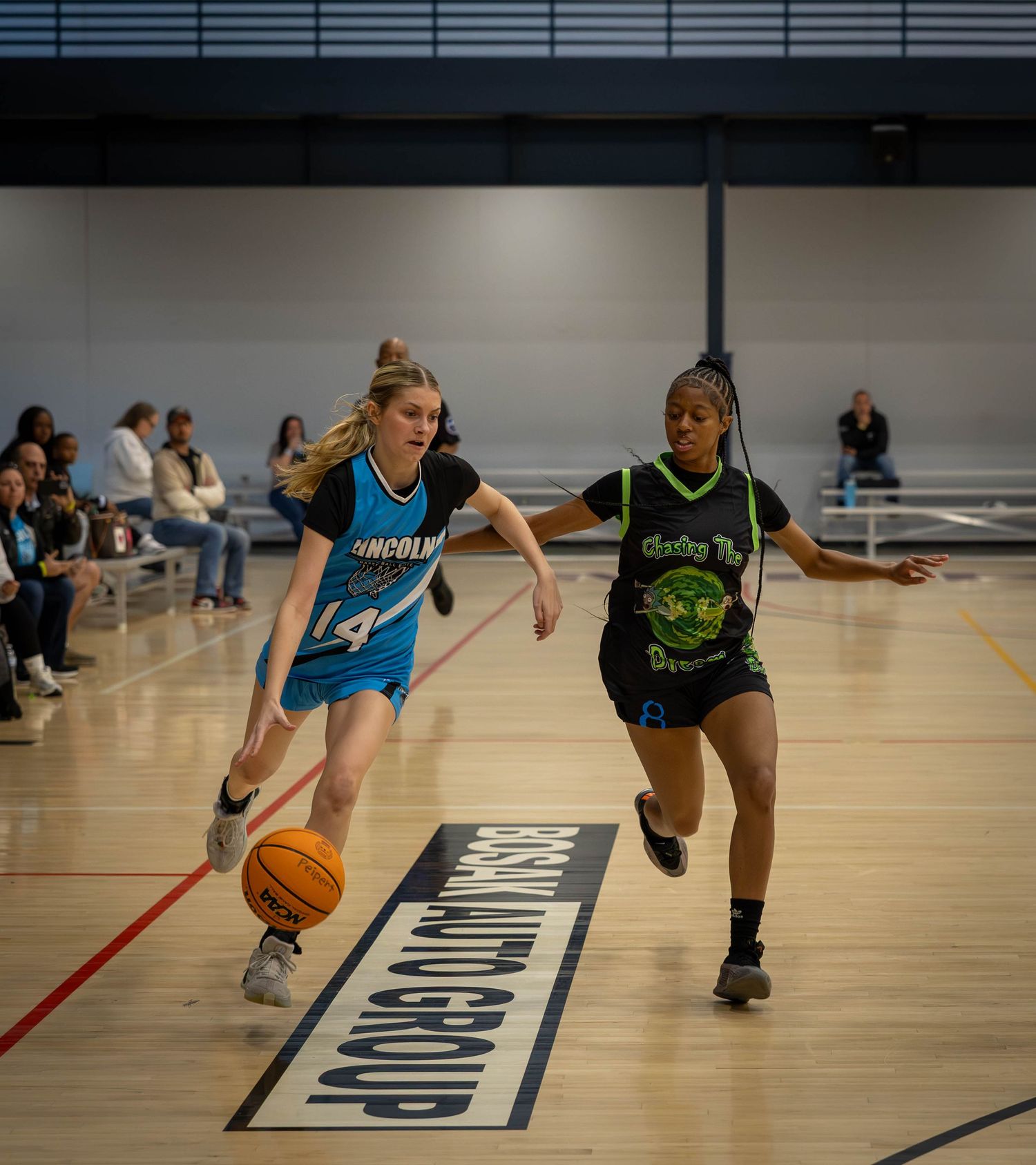 Basketball players dribble and compete during a practice game in an indoor gym court.