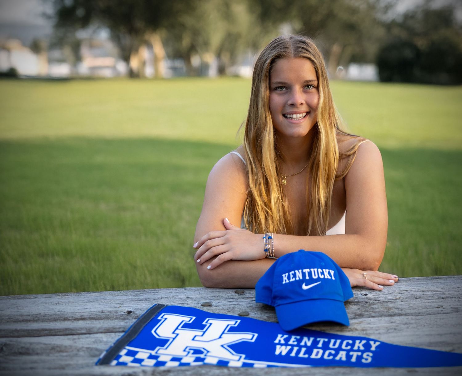 Smiling teen poses at picnic table with Kentucky Wildcats hat and pennant on a sunny day outdoors.