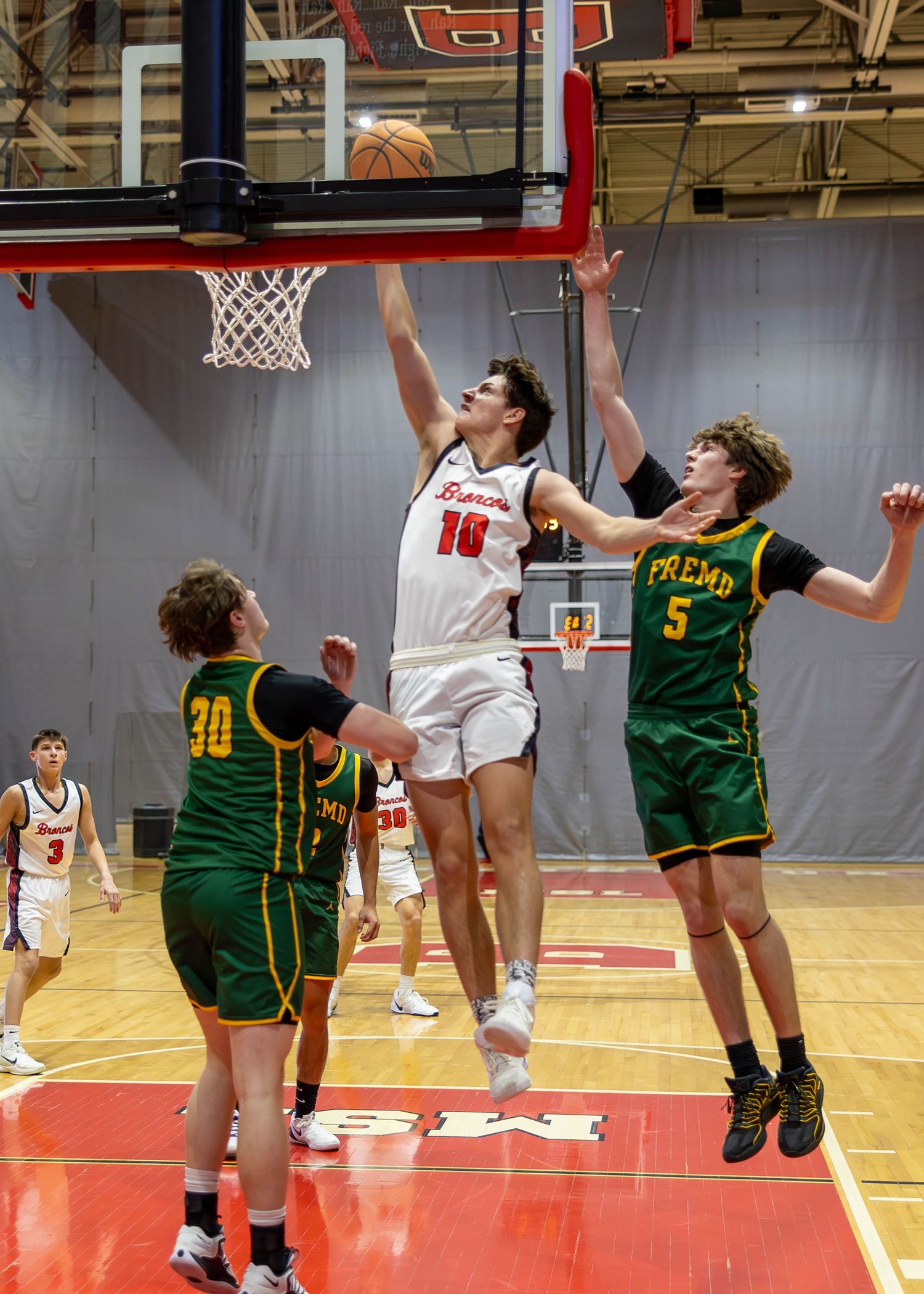High school basketball player in white uniform leaps for layup against green-uniformed Fresno defenders in indoor gym.