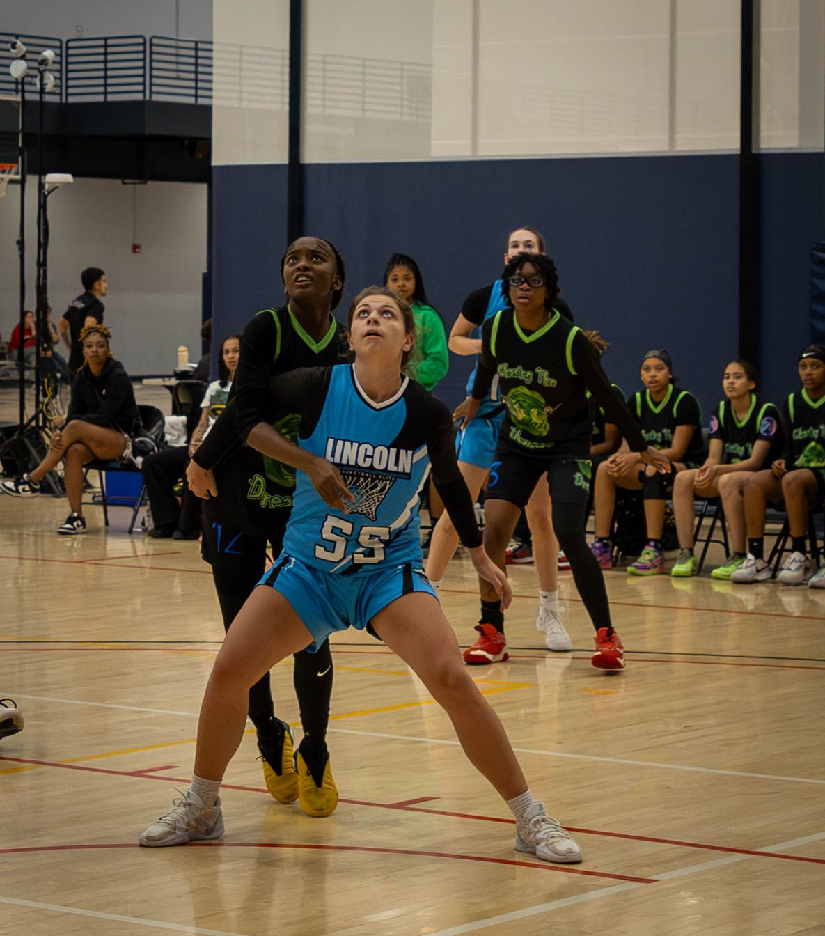 Basketball players in teal blue and black uniforms poised in defensive positions during an indoor game.