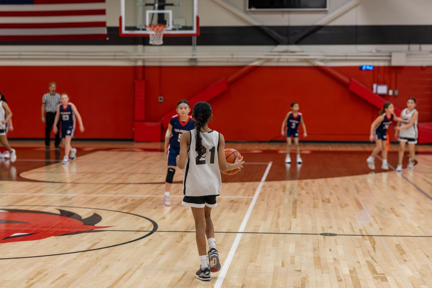 Female basketball player prepares to shoot free throw in red and white indoor gymnasium during competitive game.