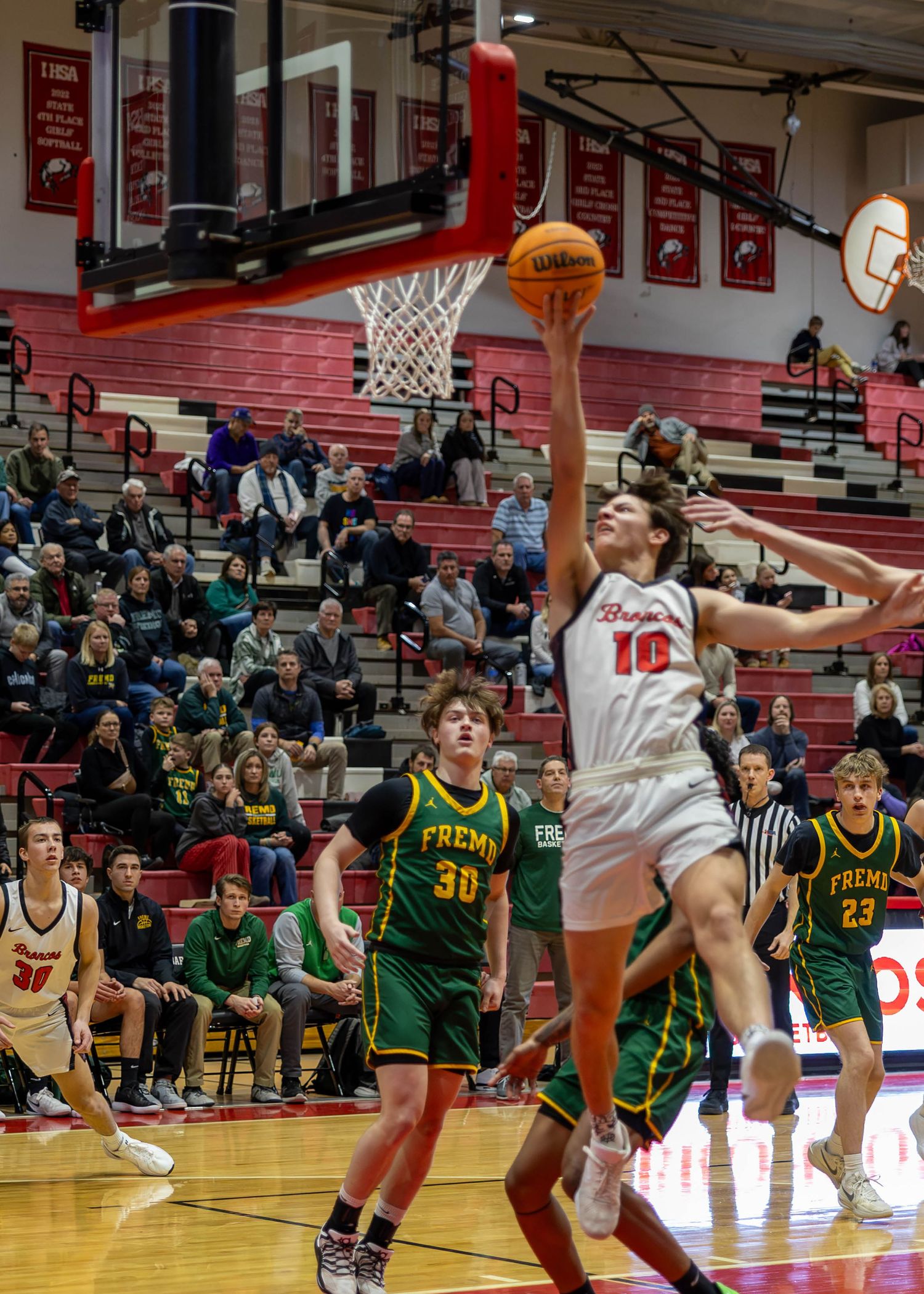 High school basketball player #10 in red attempts a layup against green-uniformed Fremont defenders in a packed gymnasium.