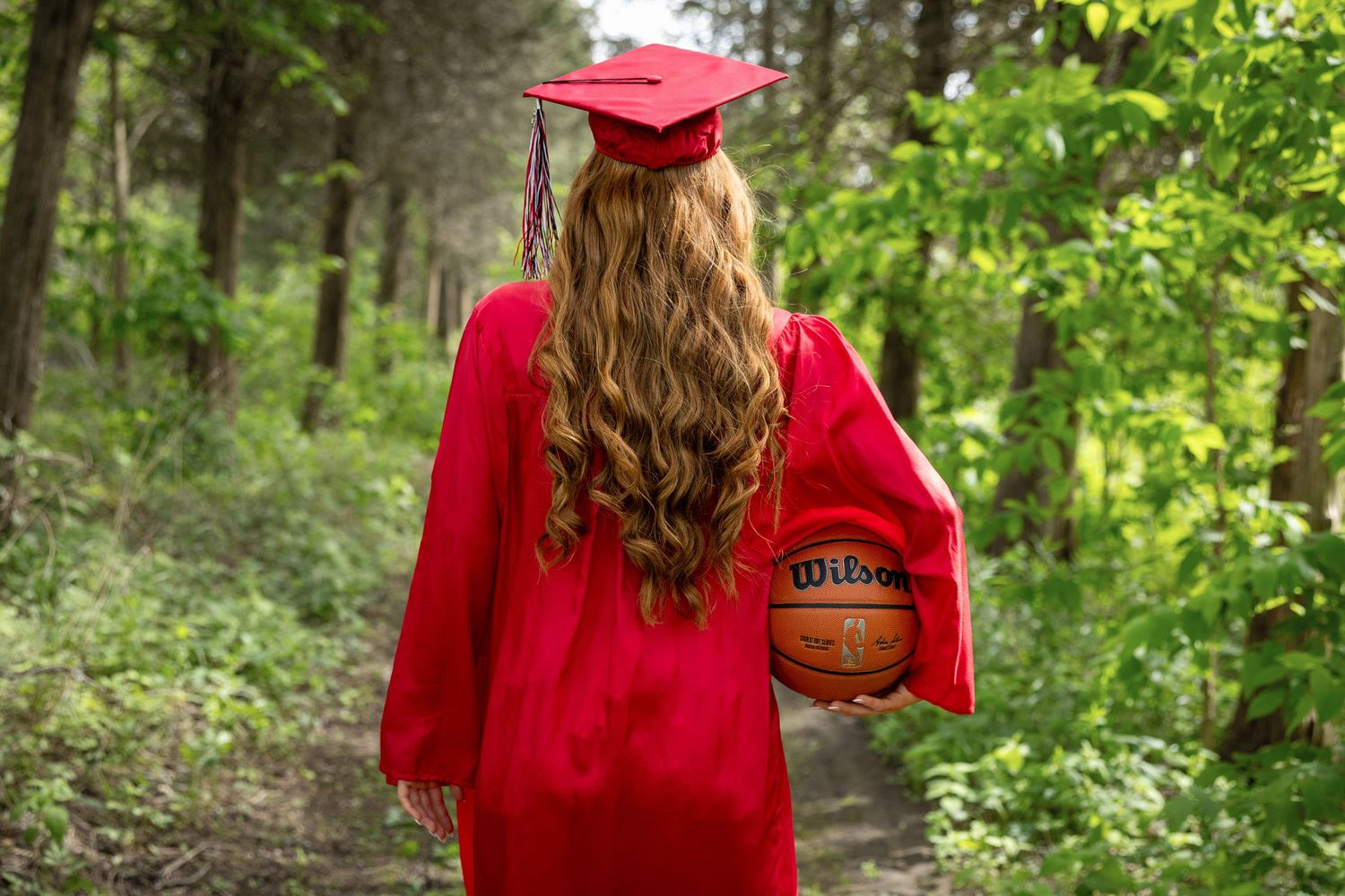 Red graduation gown and cap against lush green forest backdrop.