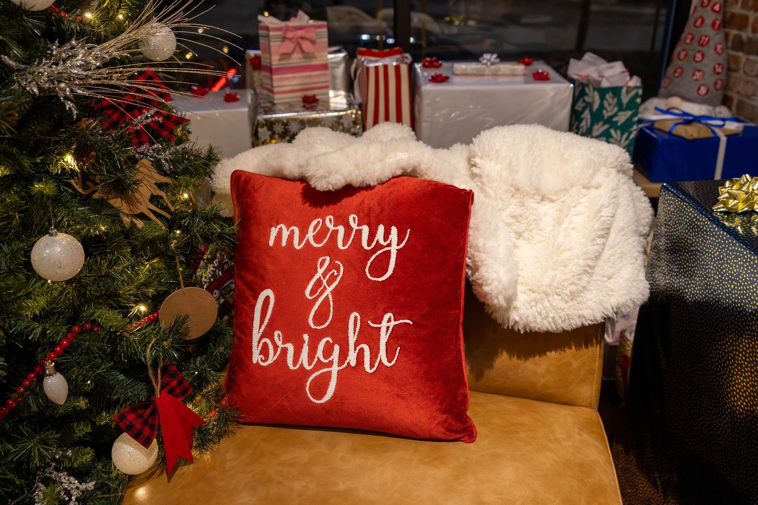 Red 'Merry & Bright' Christmas pillow beside decorated tree with wrapped gifts in festive holiday setting.