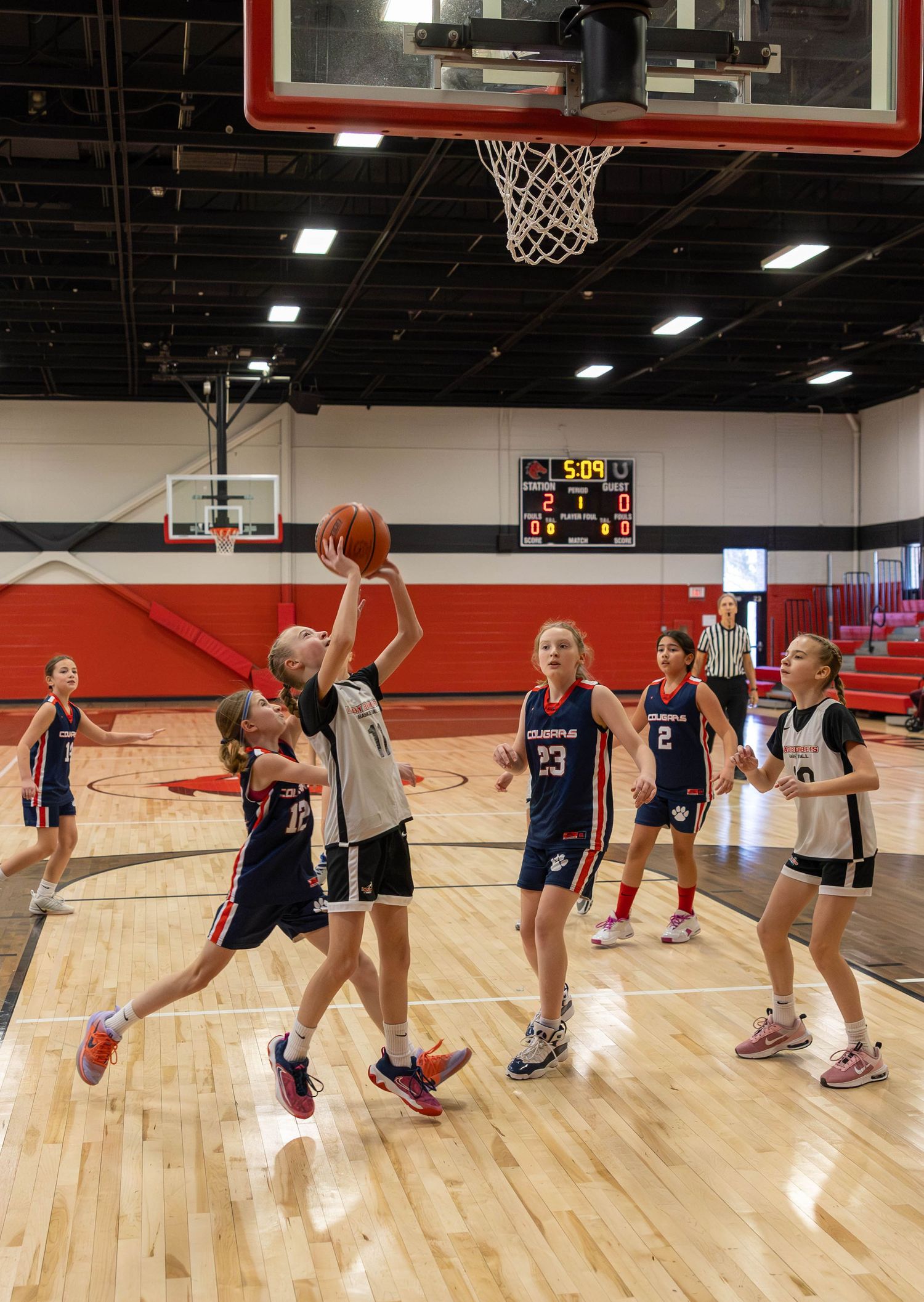 Young girls playing basketball in a gym, with one player attempting a layup while teammates and opponents watch nearby.