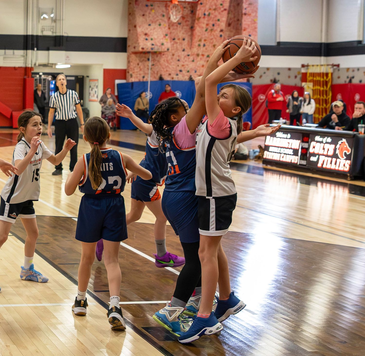 Young girls competing in an indoor youth basketball game, with one player jumping to catch the ball.