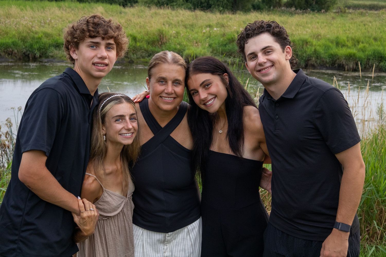 Family wearing coordinated black and white outfits pose together by pond at sunset.