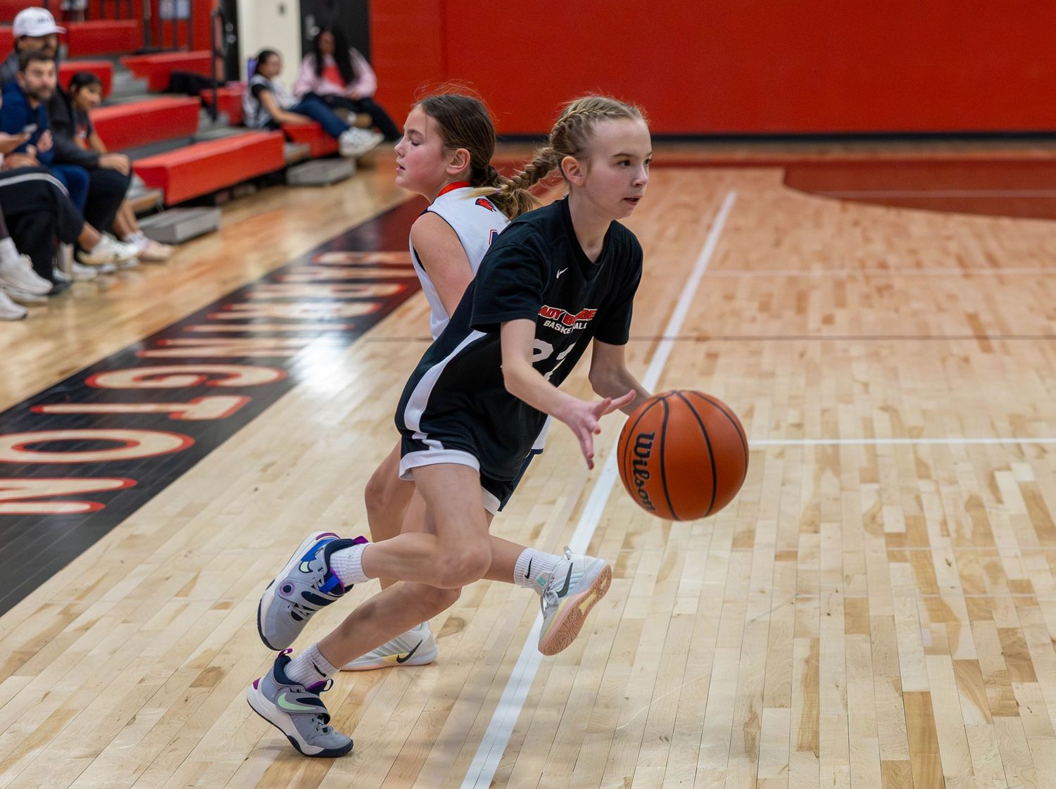 Two female basketball players compete on an indoor court, one dribbling past a defender during a high school game.
