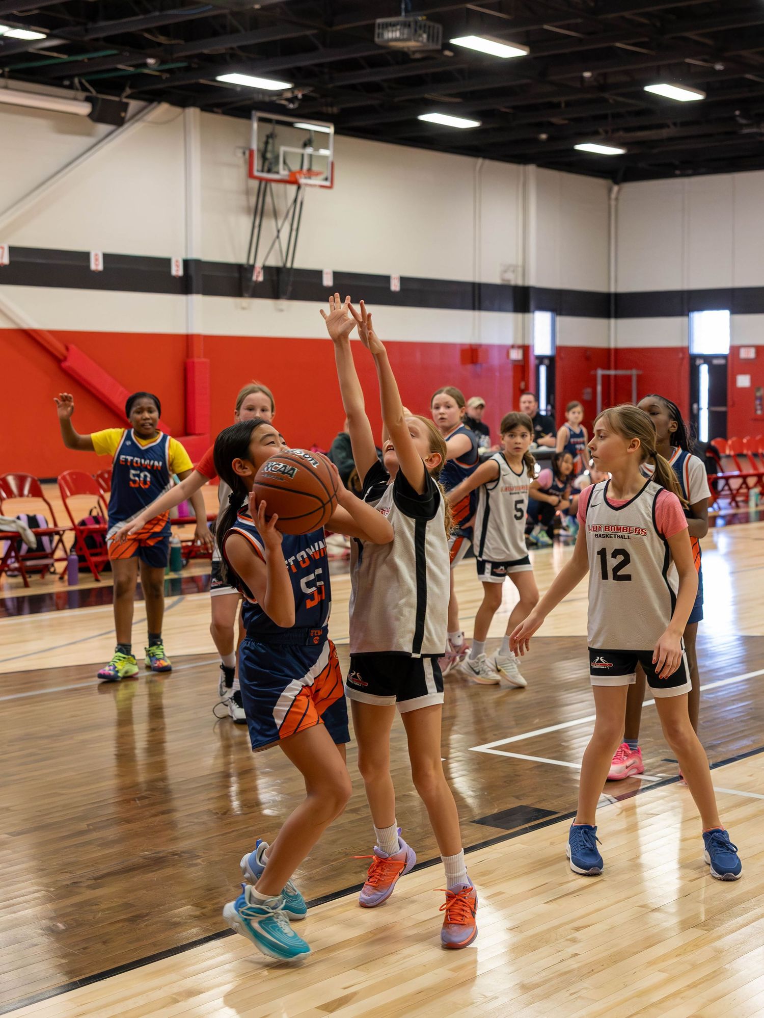 Young girls playing basketball in a gym, with one player attempting a layup while defenders reach up to block.