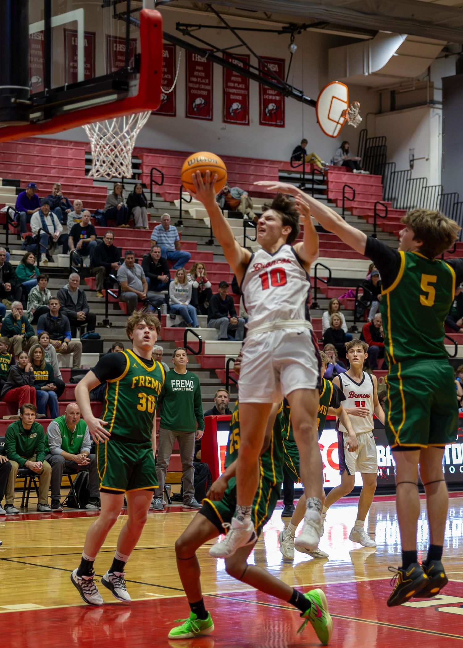High school basketball player #10 leaps for a layup surrounded by defenders in a red gymnasium.