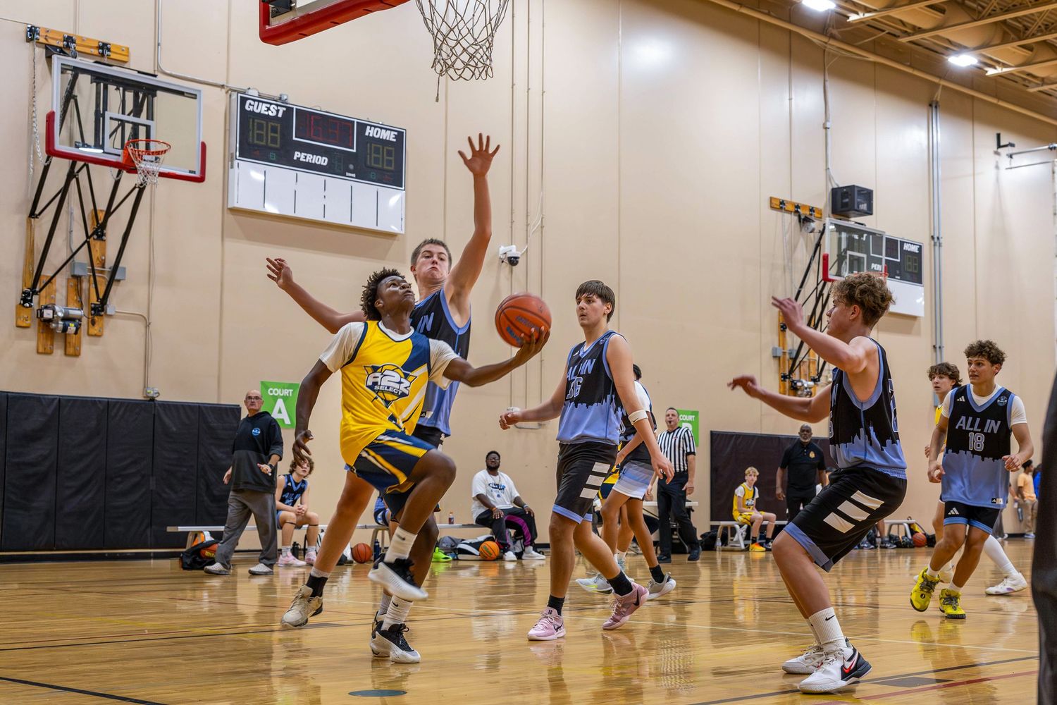 Youth basketball player in yellow drives through defenders during an intense indoor basketball game.