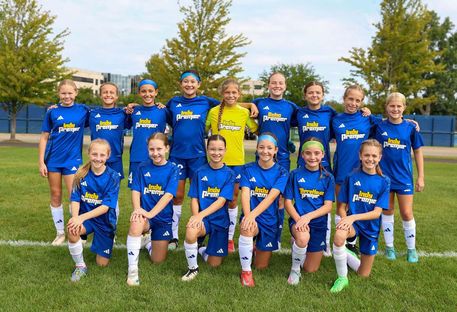 Youth soccer team wearing bright blue jerseys poses together on a grass field.