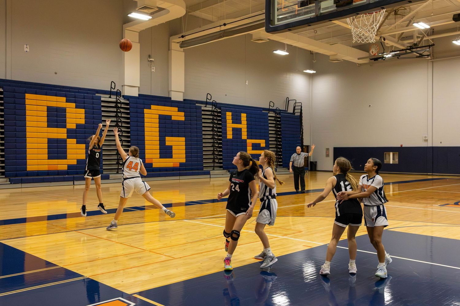 Girls high school basketball game in a gym with BGH letters on the wall, player shooting toward the hoop.