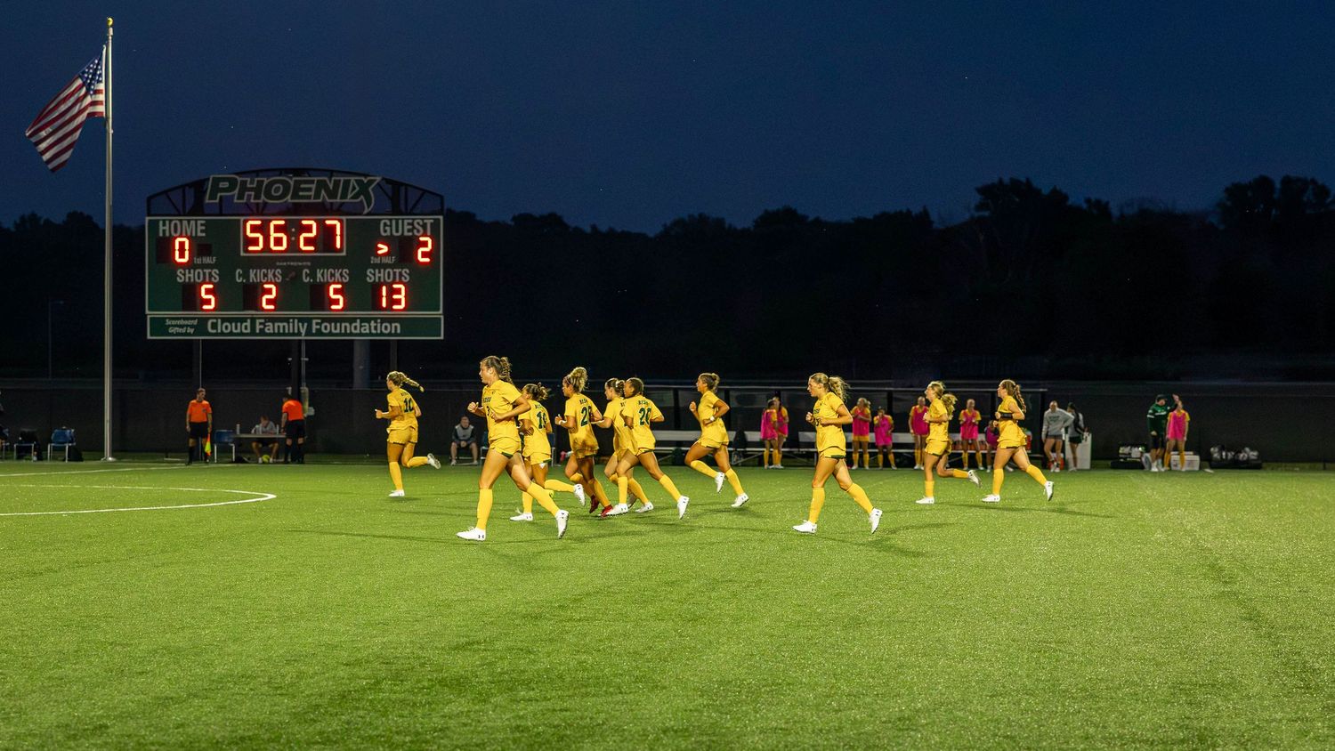Soccer players in yellow uniforms celebrate on a green field at night under stadium lights.