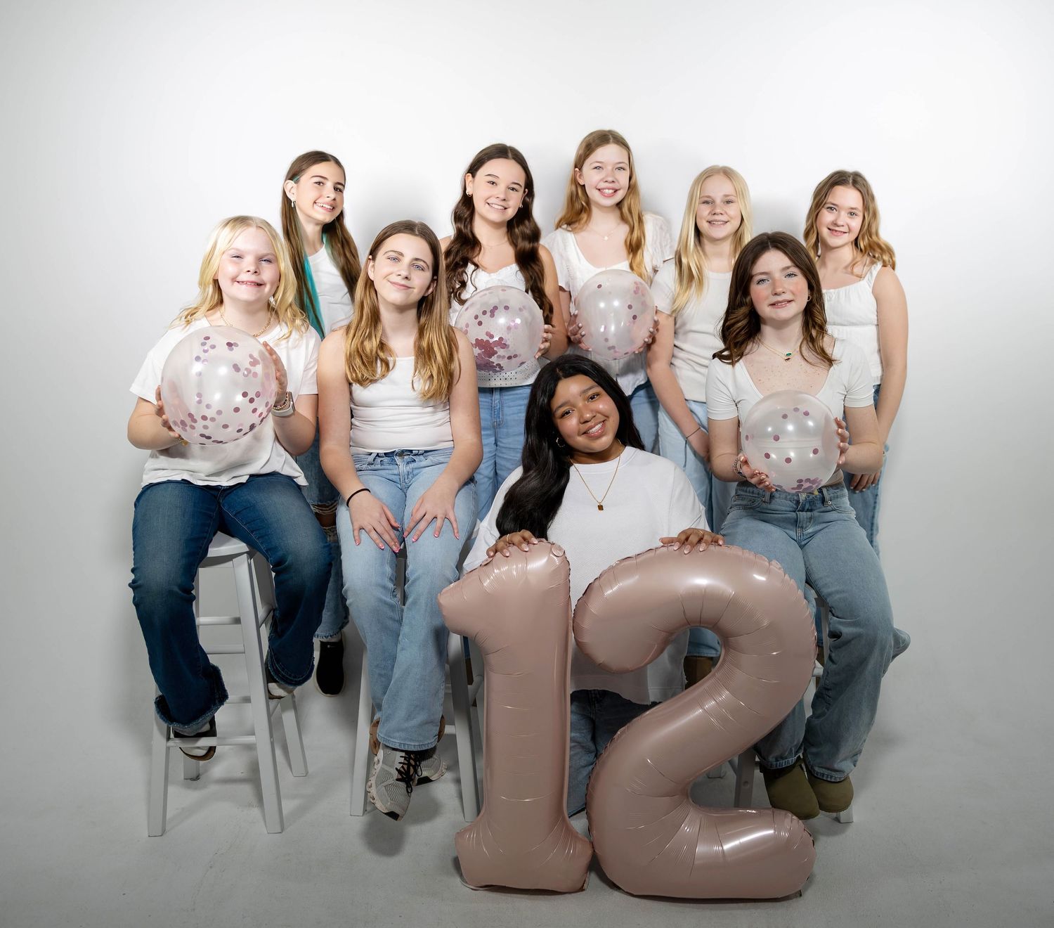 Group of girls posing with number 12 balloons and disco ball balloons for a birthday celebration photo.