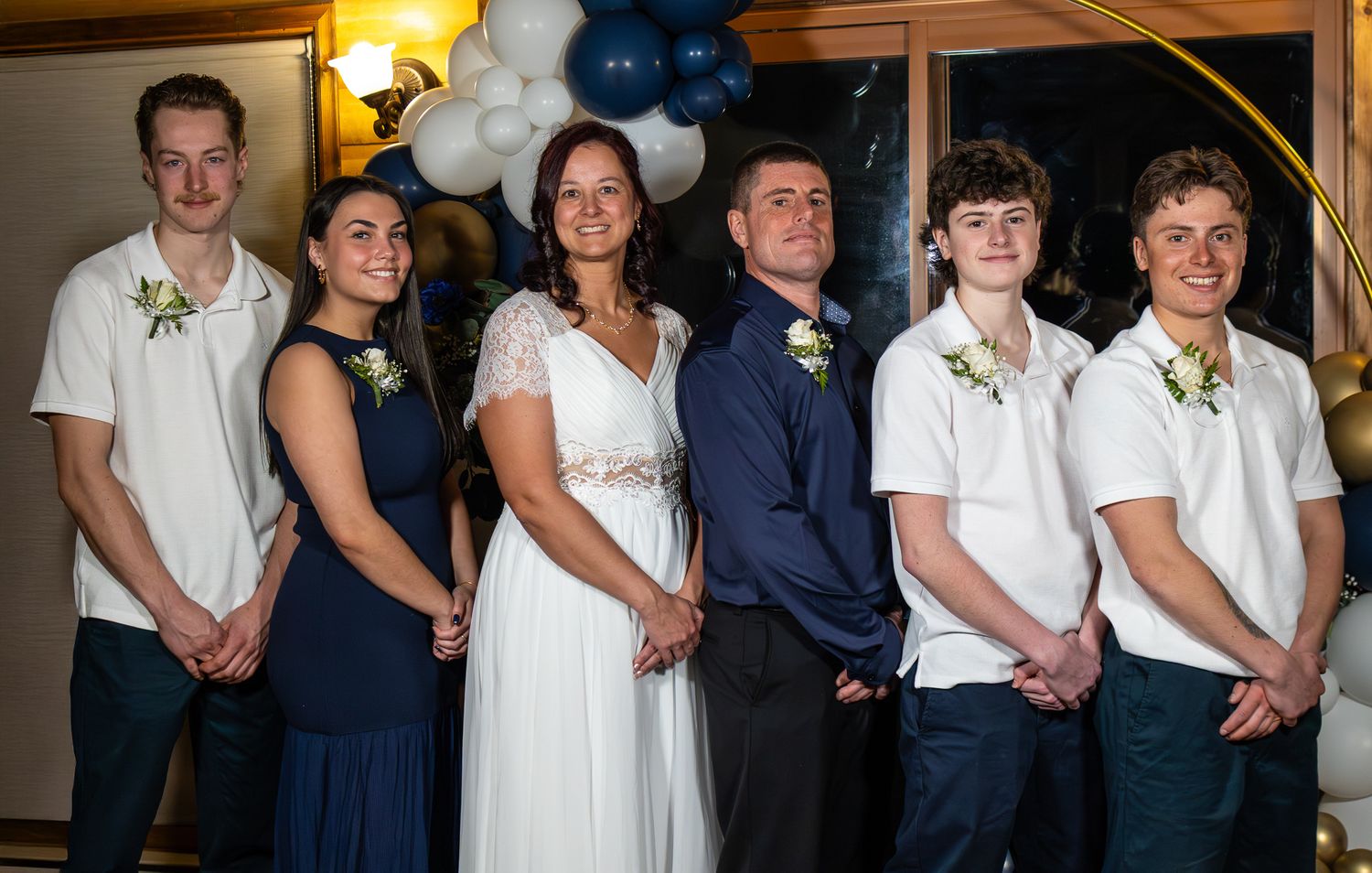 Wedding party of six poses together with bride in white gown and guests in navy and white attire.