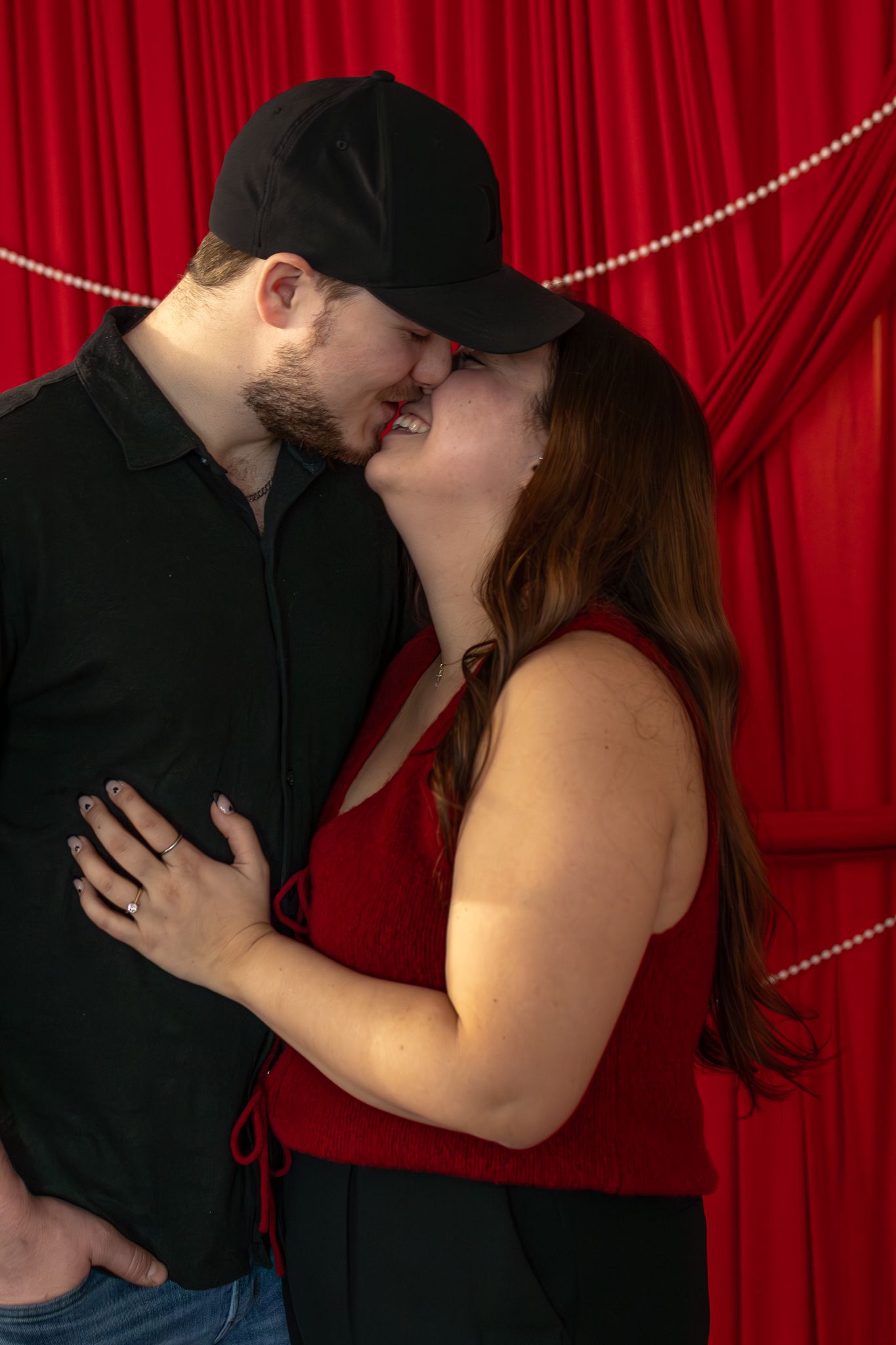 Couple sharing romantic almost-kiss moment in front of elegant red curtain backdrop.