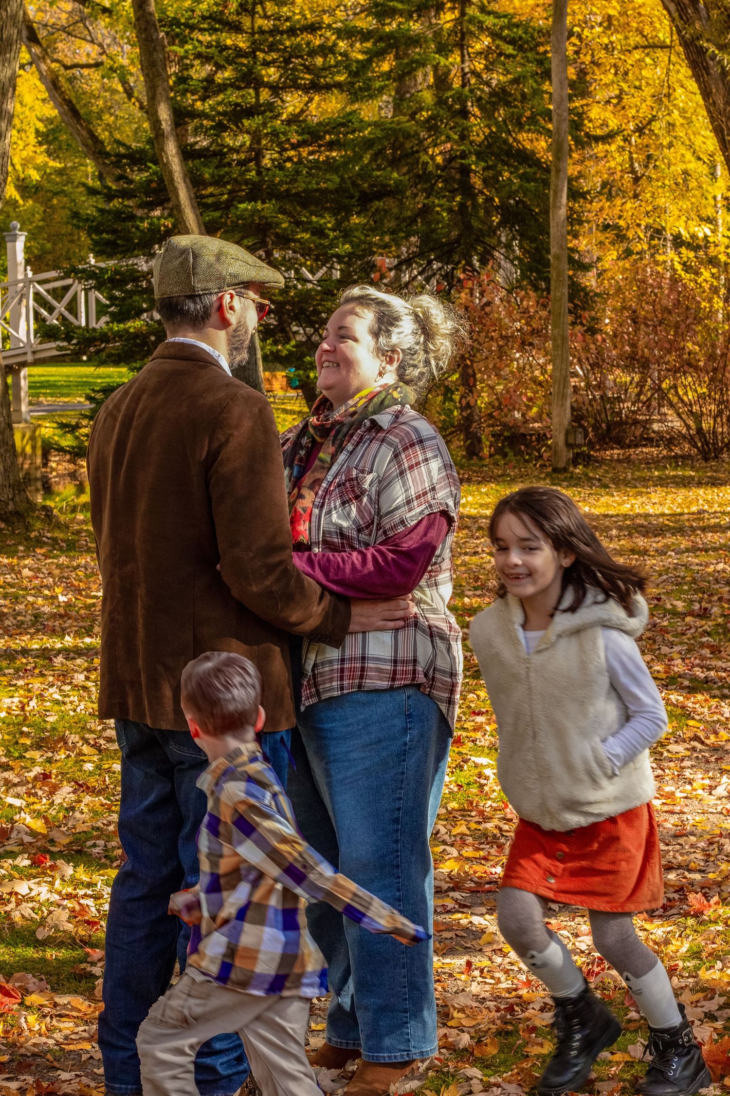 Family of four playing and laughing together among colorful fallen leaves in an autumn park.