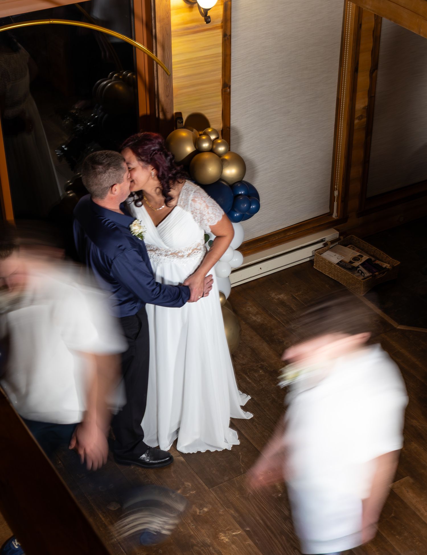 Bride and groom share a first kiss on the dance floor surrounded by navy and gold balloons at their wedding reception.