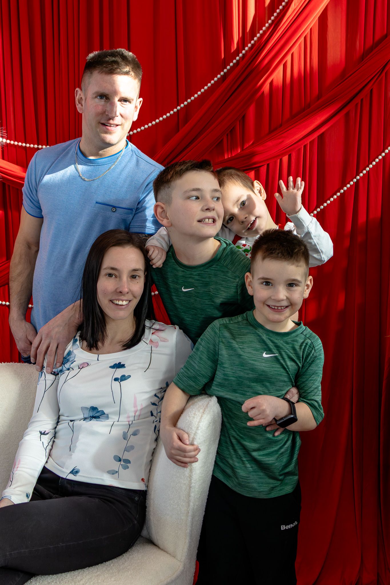 Family of five smiling and posing casually in front of a bright red curtain background.