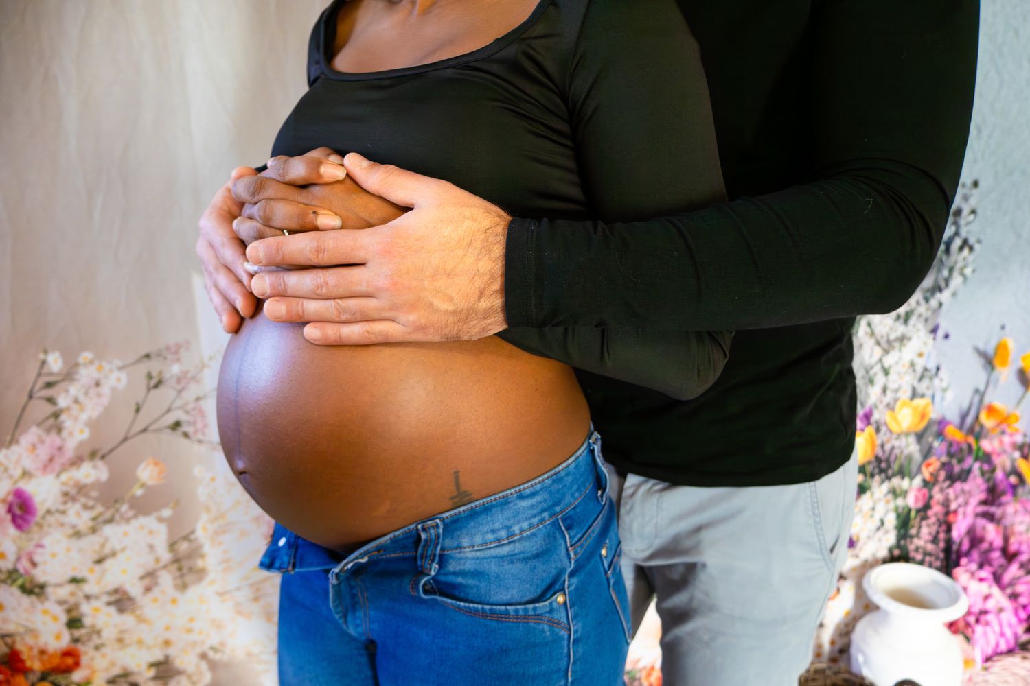 Close-up of pregnant belly with partners hands gently cradling bump during maternity photography session.