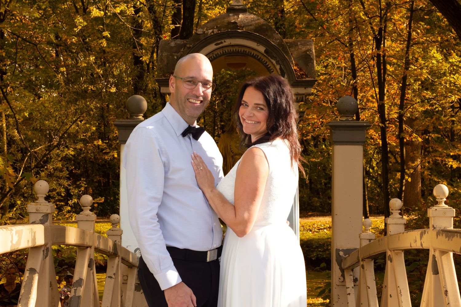 Happy wedding couple posing together on a bridge surrounded by vibrant golden autumn trees.
