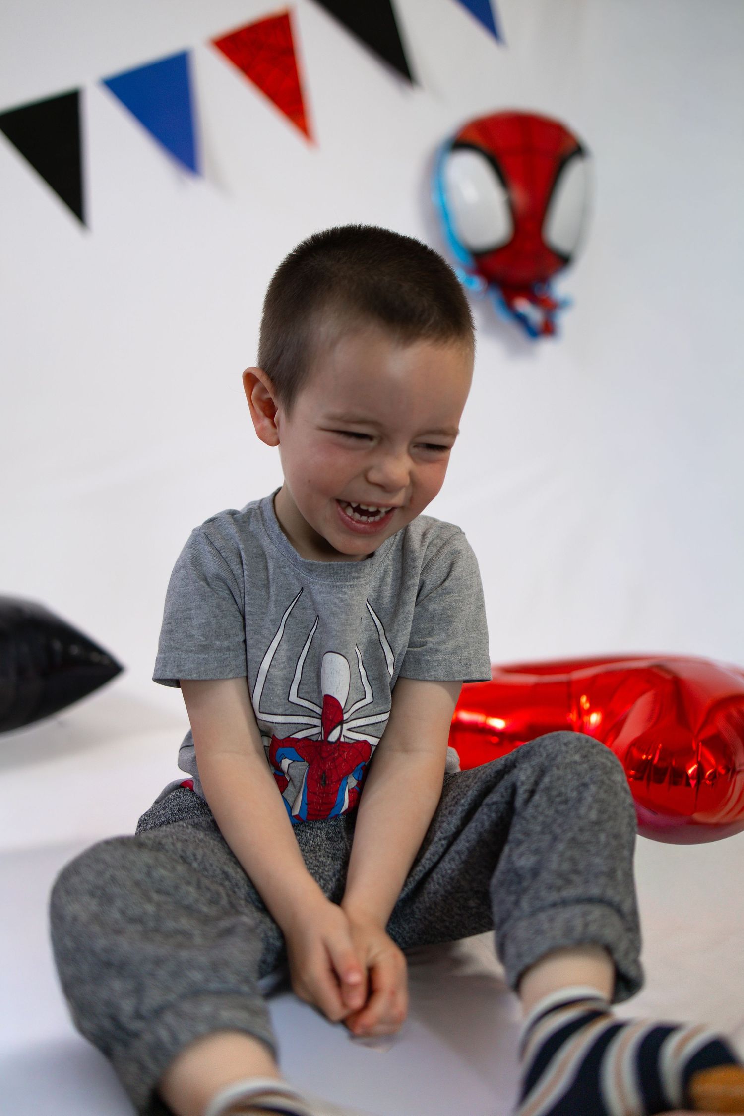 Happy young boy in Spiderman shirt laughing at birthday party with red balloon and Spiderman decorations.