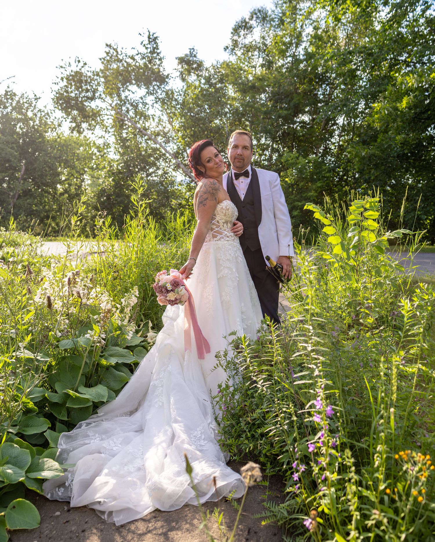 A bride and groom pose romantically among lush green wildflowers and plants on their outdoor wedding day.