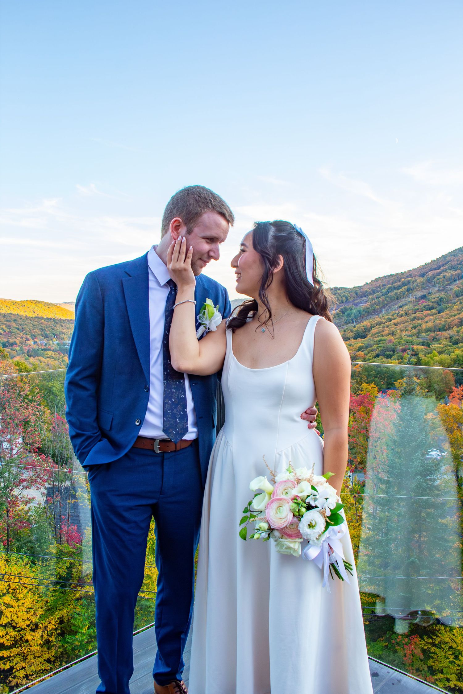 Bride and groom share a romantic moment on a scenic overlook with colorful autumn foliage and mountains behind them.
