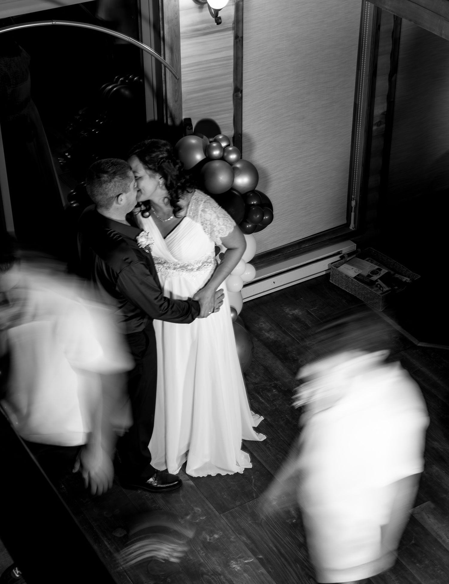 Black and white aerial shot of bride and groom kissing on dance floor surrounded by dancing guests.