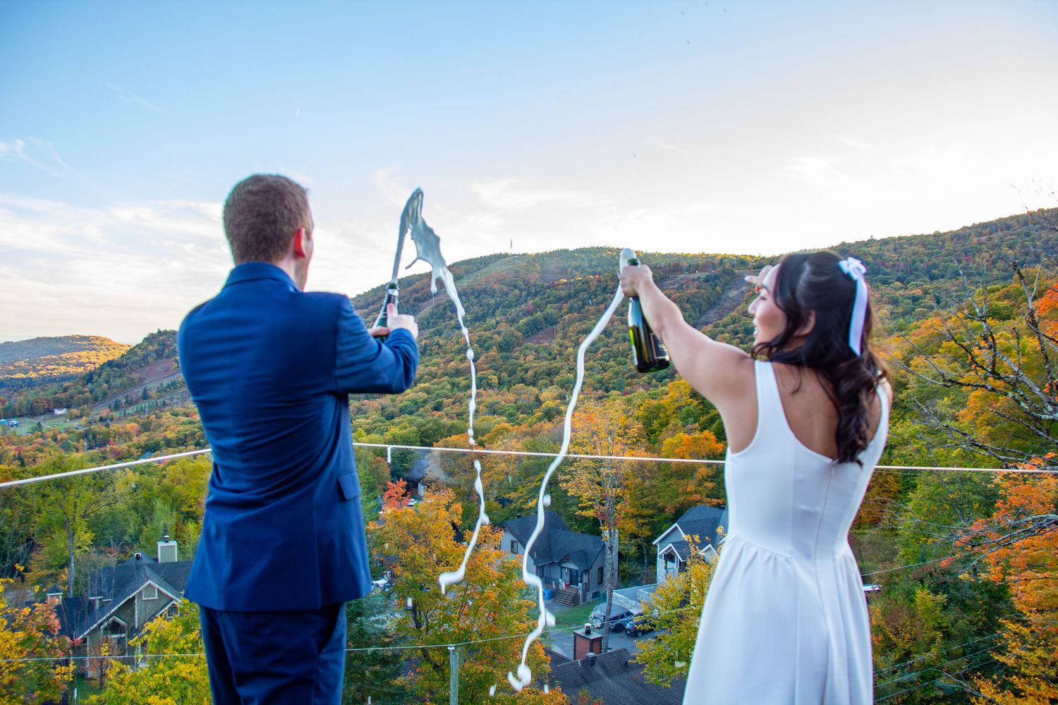 Bride and groom releasing ribbon streamers on a balcony with autumn mountain landscape.