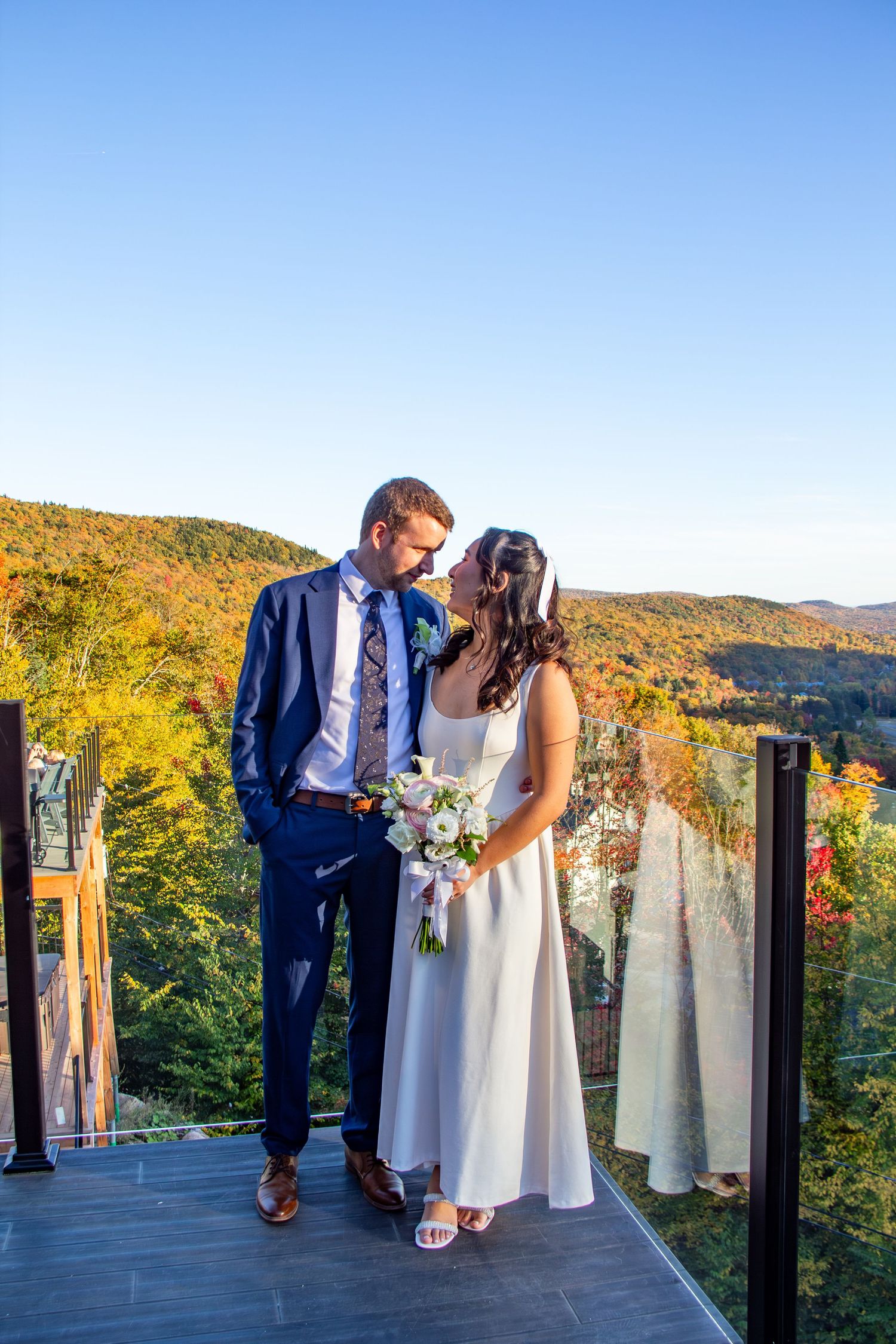 Bride and groom sharing a tender moment on a deck with colorful autumn mountains.
