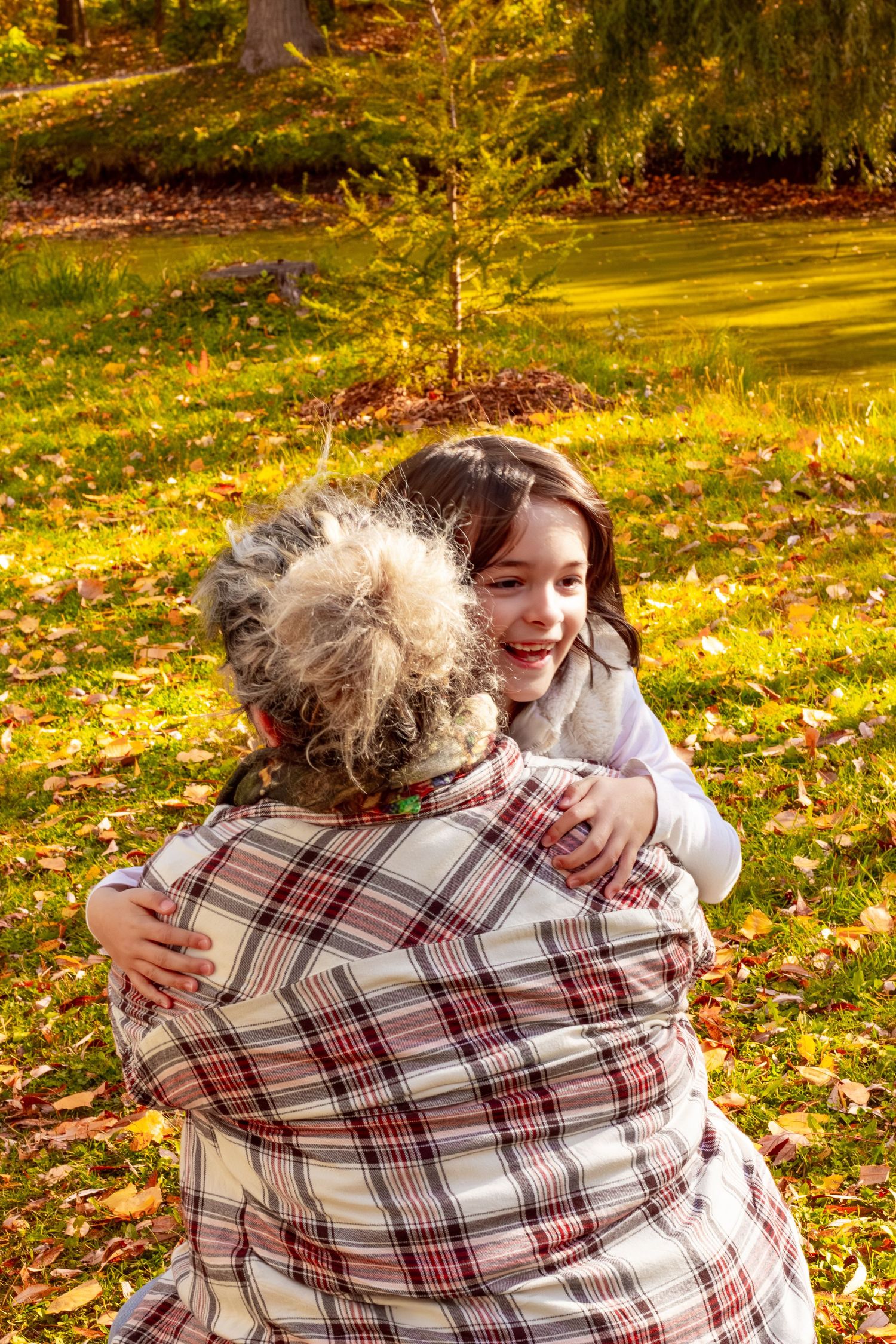 Smiling girl embracing a woman in a plaid shirt in a bright autumn park.