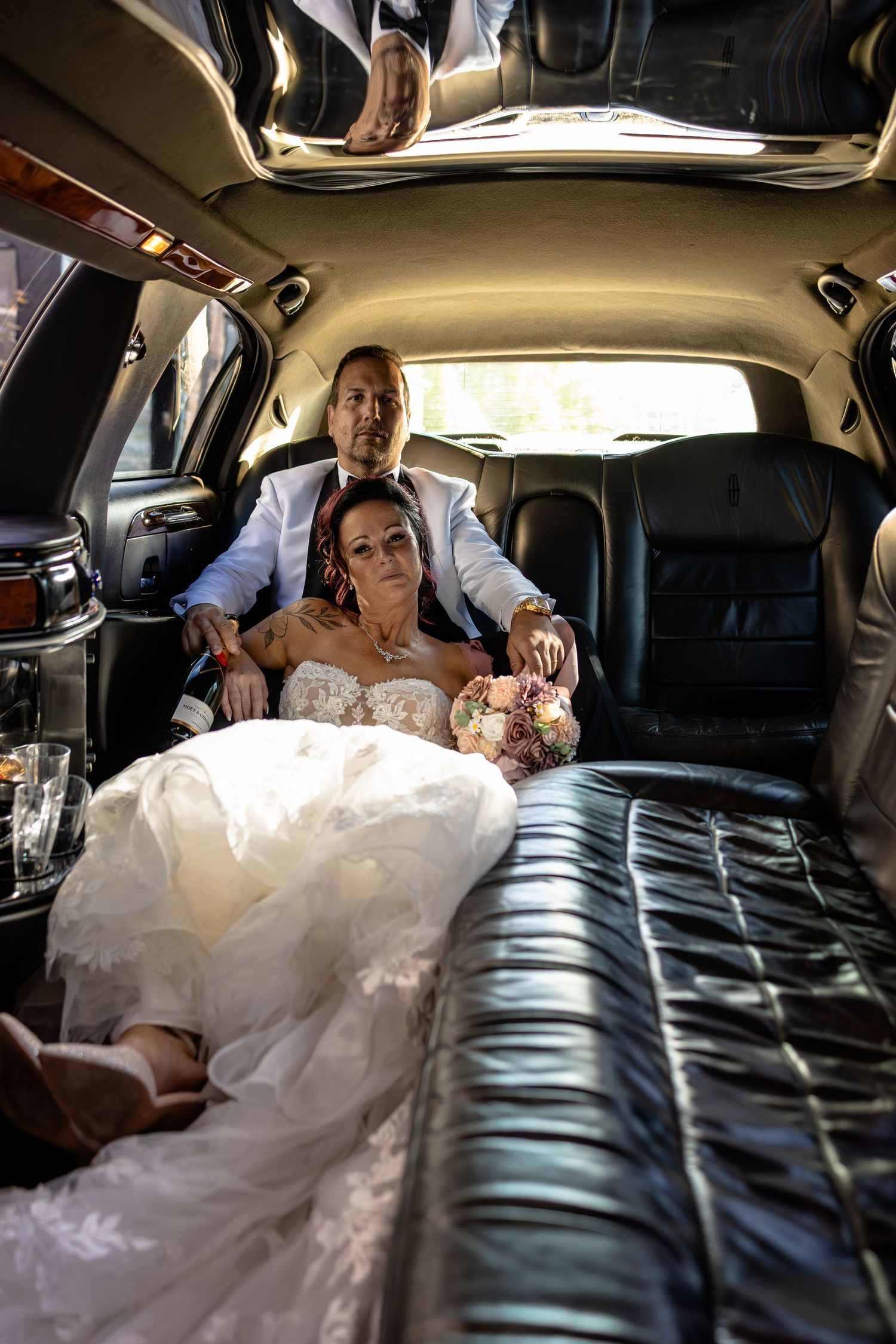Bride and groom sitting together in a luxurious black leather limousine on their wedding day, bride holding a bouquet.