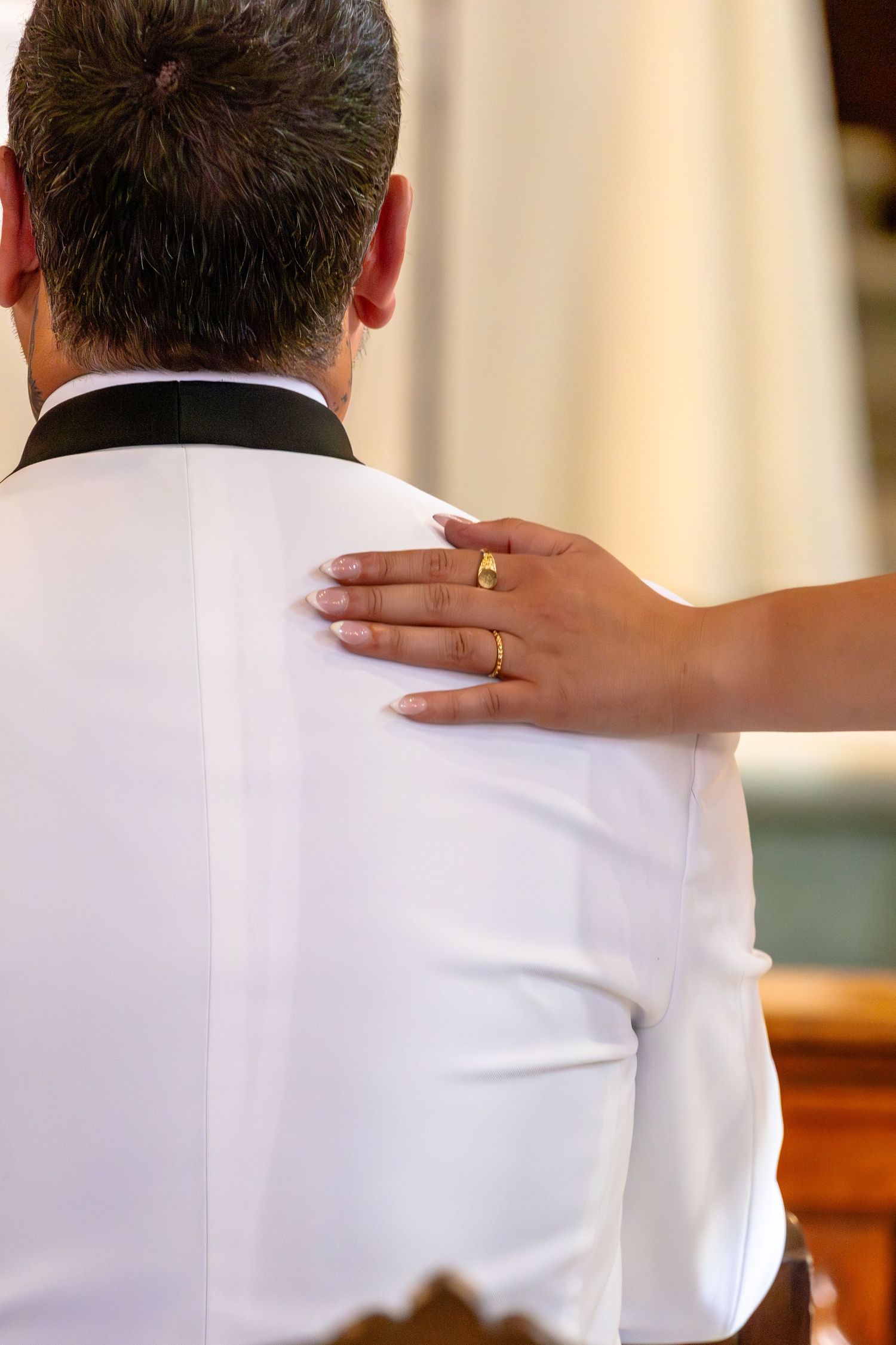 Bride placing her hand on groom's shoulder during wedding ceremony, wearing a gold ring on her finger.
