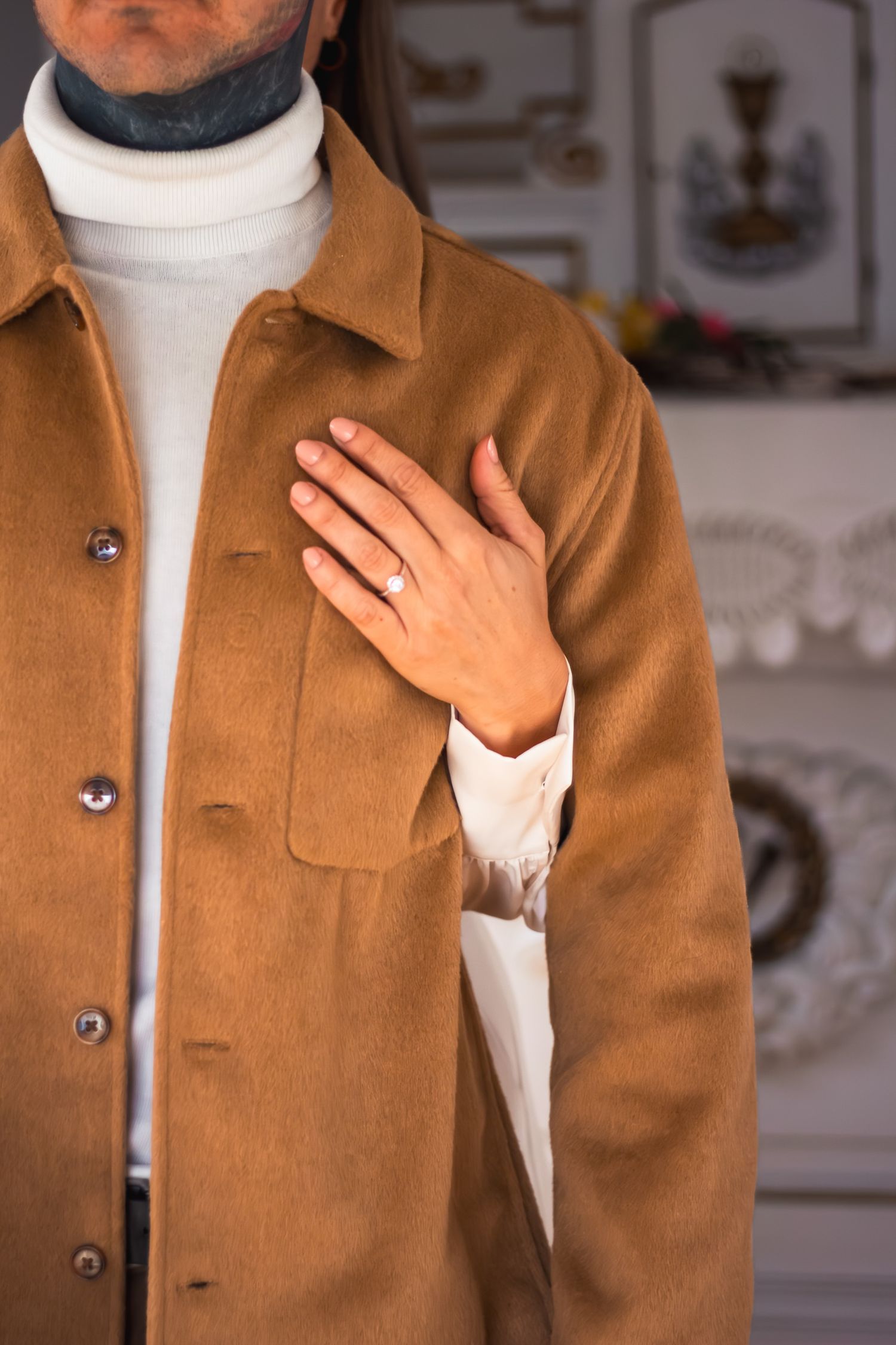 Close-up of brides hand with diamond engagement ring resting on grooms camel-colored wool jacket.