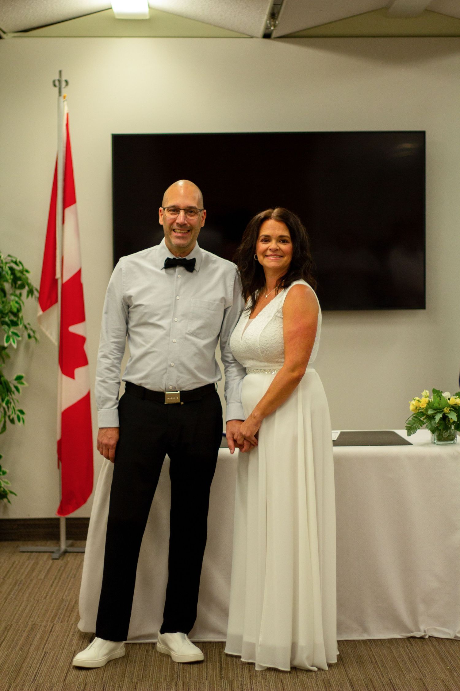 Bride and groom hold hands standing before Canadian flag during intimate civil wedding ceremony.