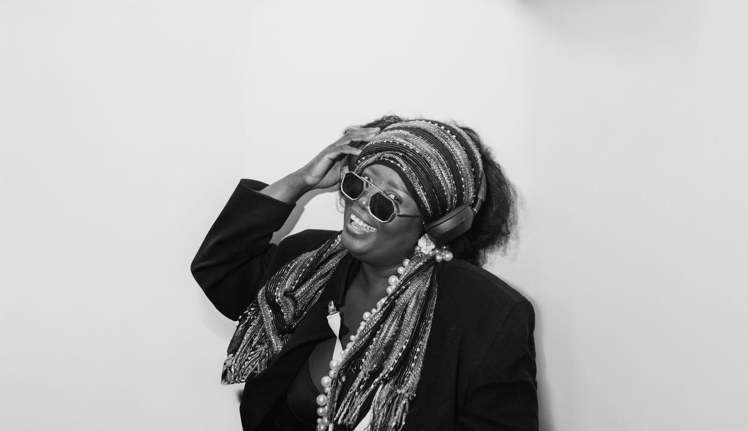 Black and white portrait of a smiling woman with colorful braids and round sunglasses against a white background.