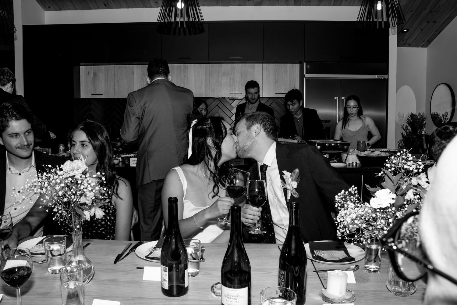 Bride and groom share an intimate moment at their wedding reception dinner table in black and white.
