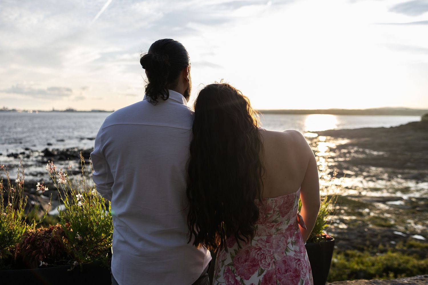 Couple standing together watching a romantic sunset over the ocean from a rocky coastal viewpoint.