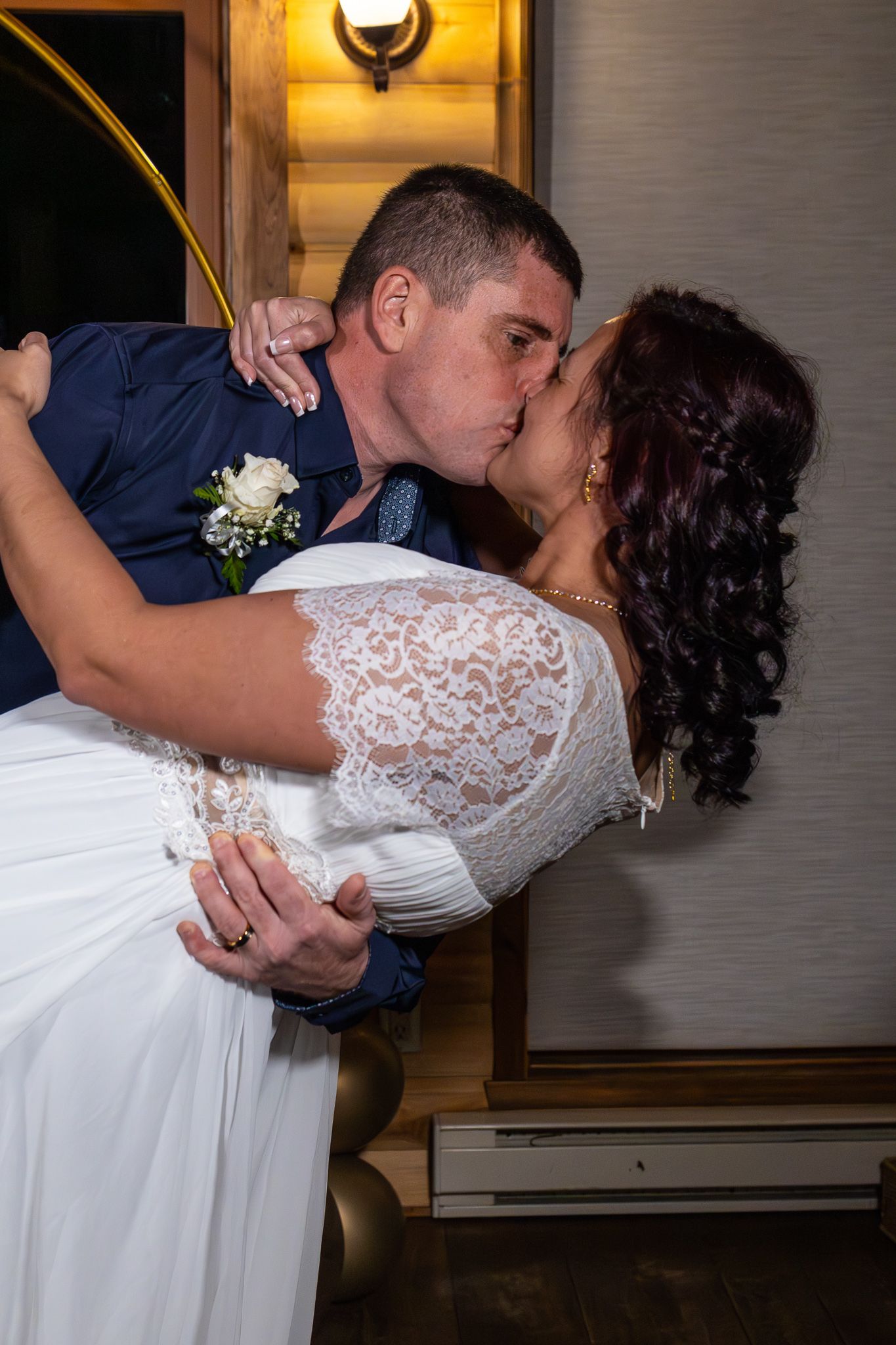 Groom dips bride in a romantic kiss in front of a gold circular arch at their wedding reception.