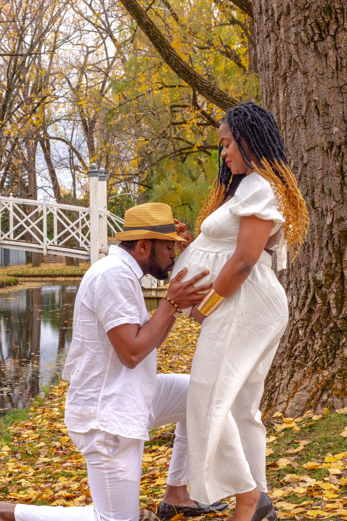 Man kneeling and kissing pregnant woman's belly in a romantic autumn park maternity photo session.