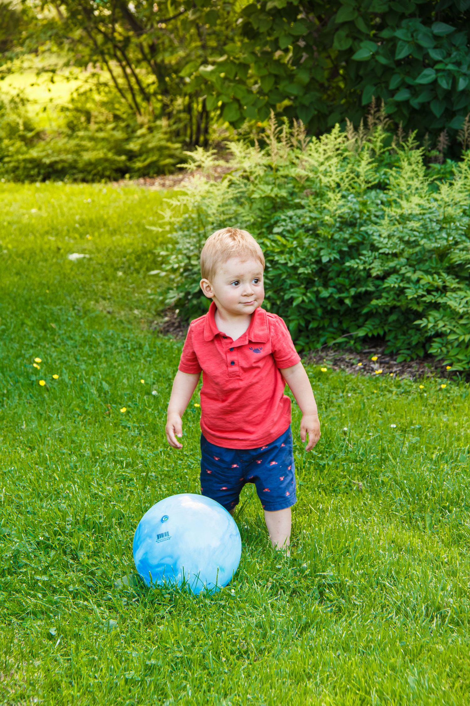 Jeune enfant jouant avec un ballon bleu sur l’herbe dans un parc.