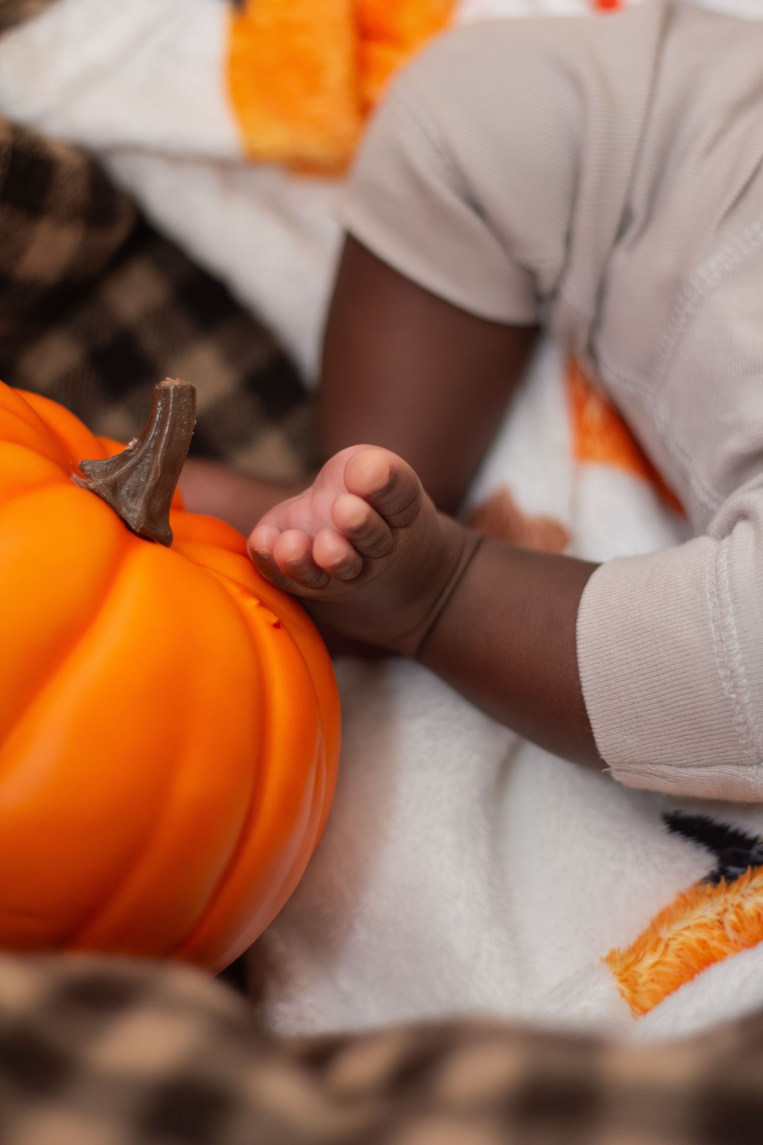 Close-up of a baby's hand touching a bright orange pumpkin on a white blanket.