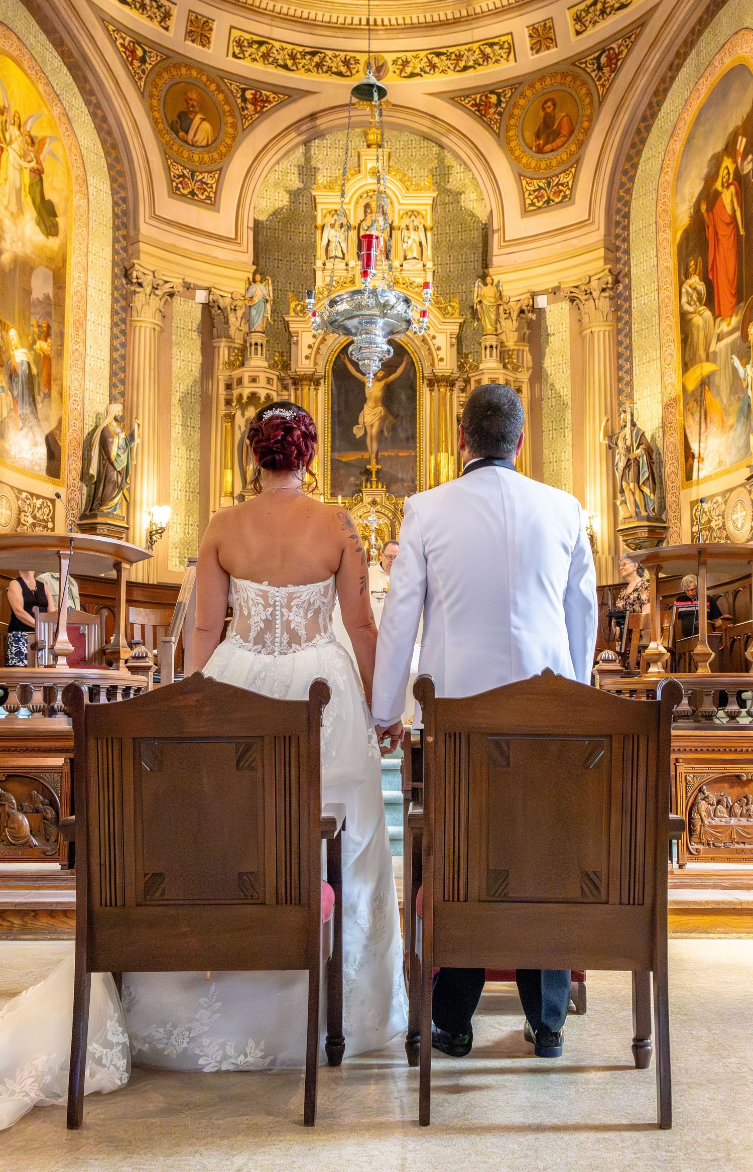 A bride and groom hold hands at the altar of an ornate golden church during their wedding ceremony.