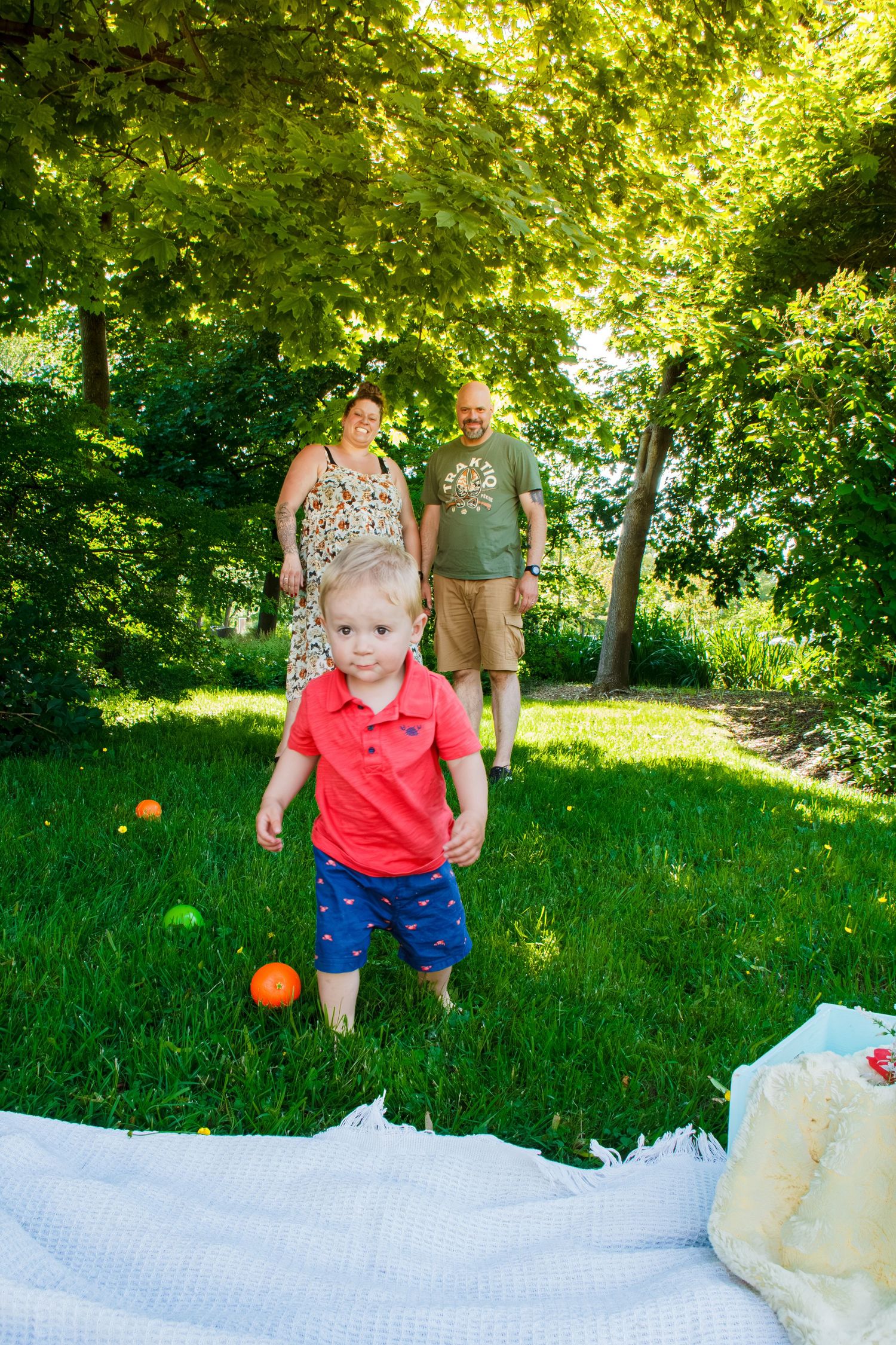 Jeune garçon courant sur l’herbe devant ses parents pendant une séance photo familiale en plein air.