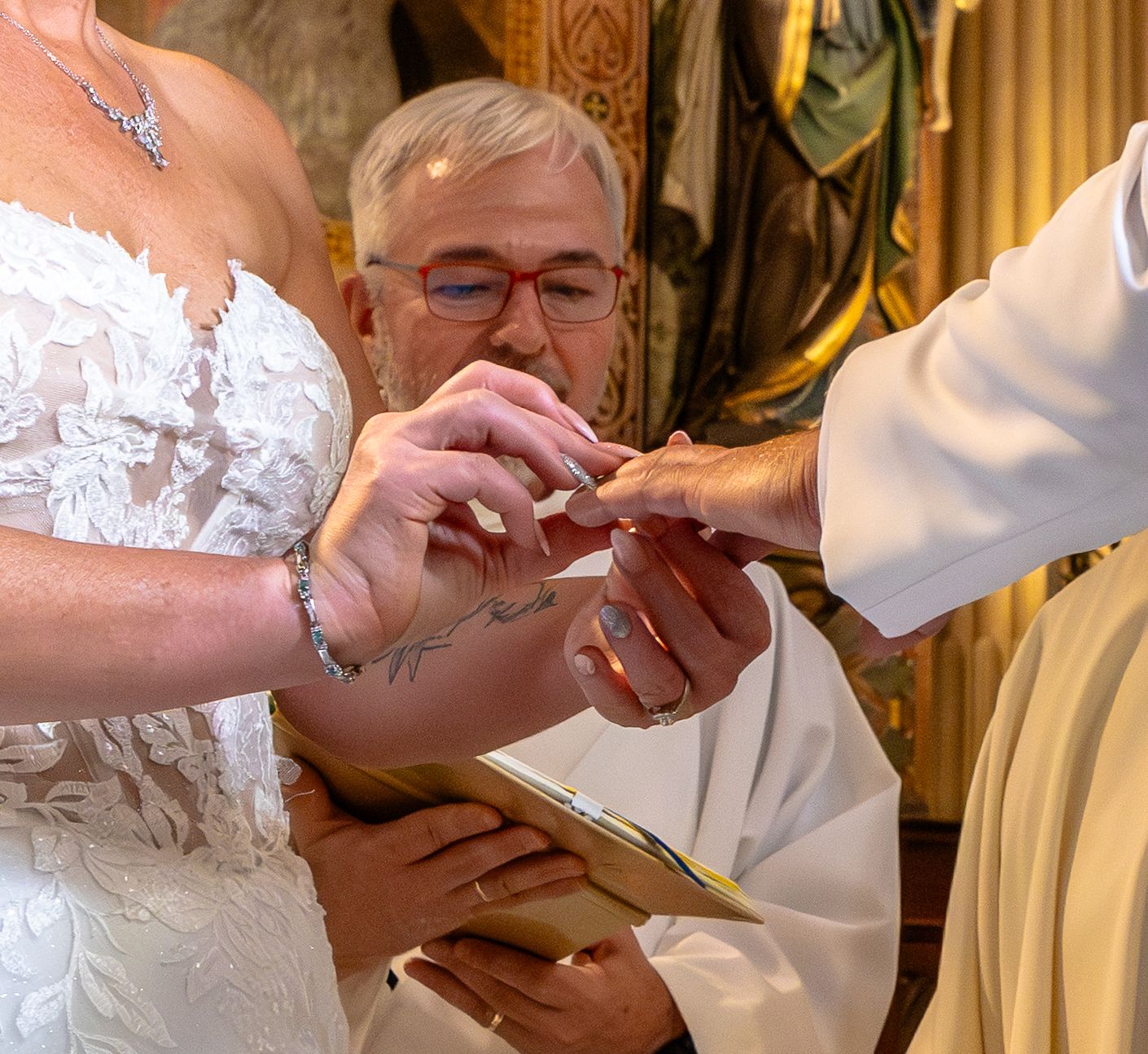 Bride and groom exchanging wedding rings during a church ceremony, officiant assisting with ring placement.
