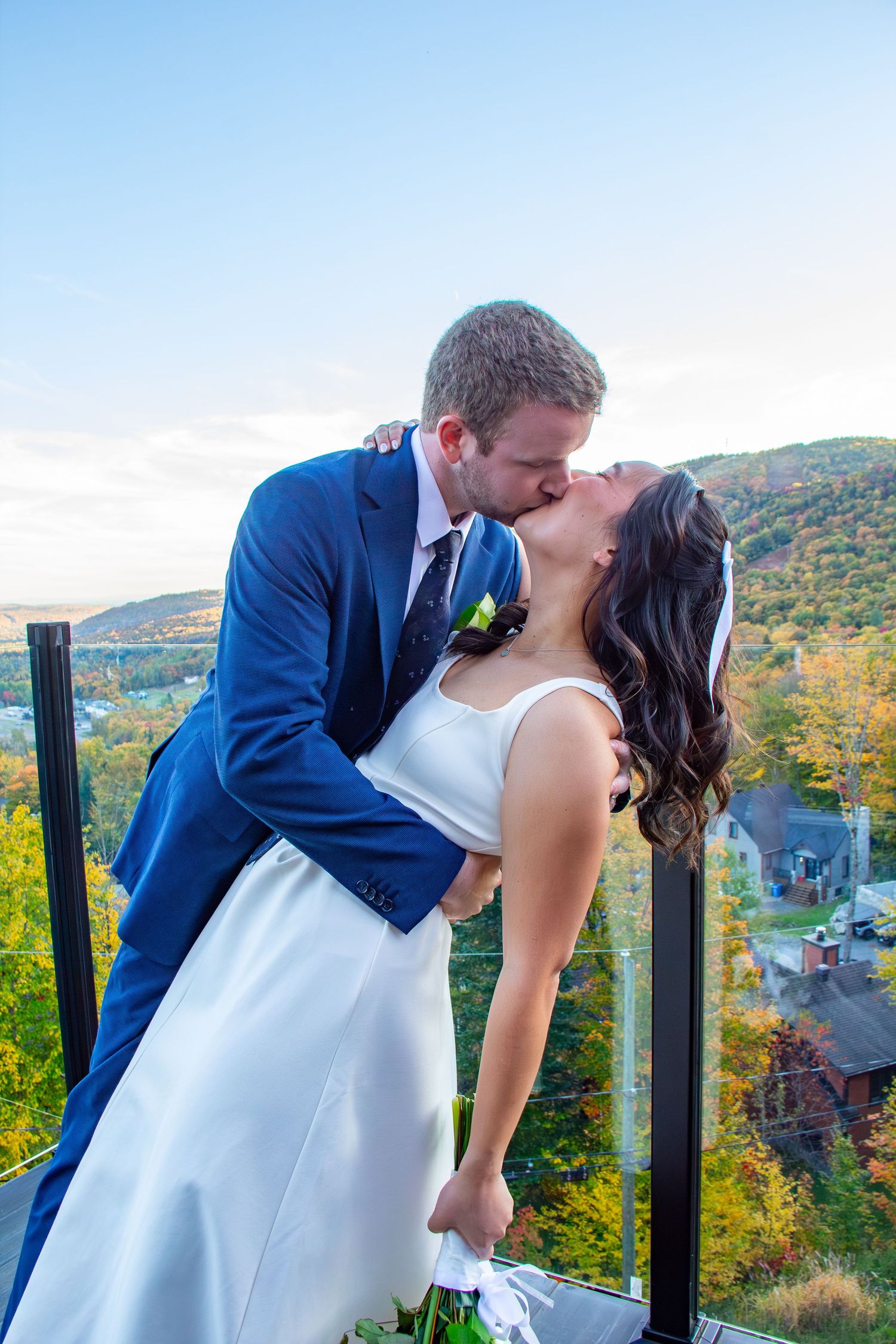 Bride and groom sharing a romantic dip kiss on a balcony with fall foliage backdrop.